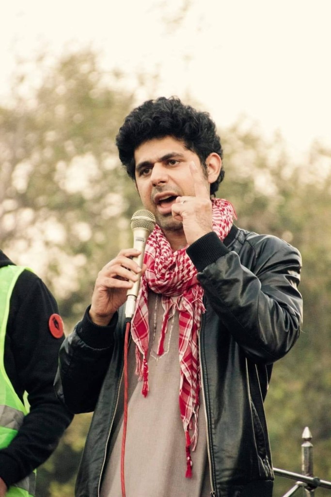 Man speaking into a microphone with his index finger raised.