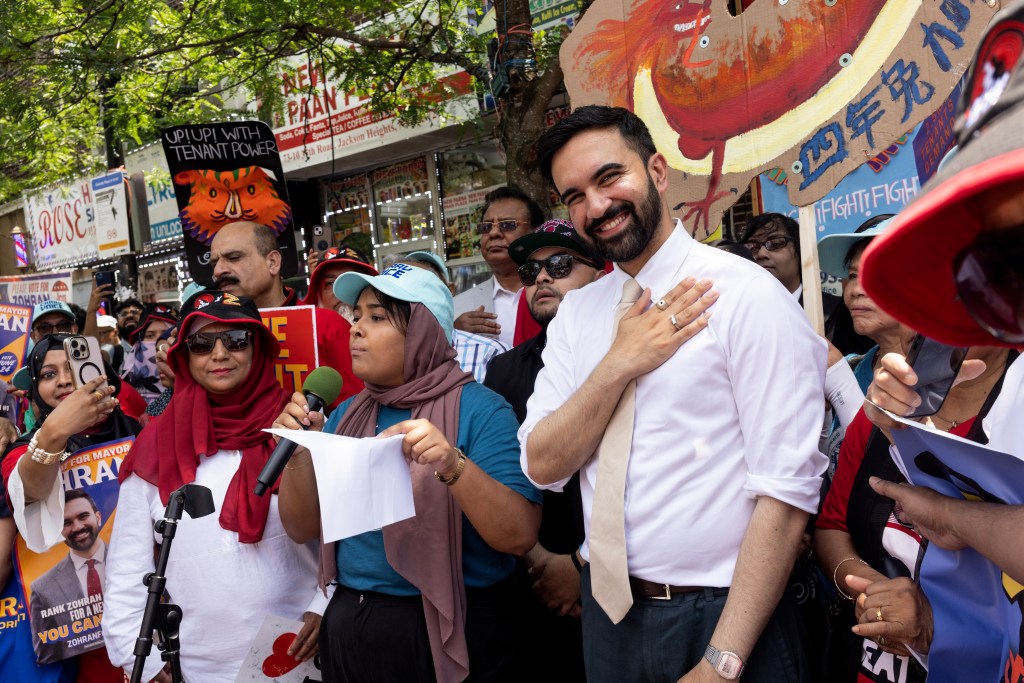 Candidate Zohran Mamdani smiling with his hand on his chest at a campaign rally in Jackson Heights.