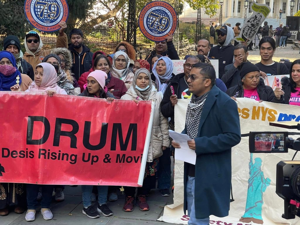 A group of people demonstrating outdoors, holding a red banner that reads 