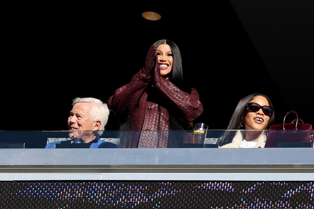 Cardi B acknowledging the crowd at a football game, with a man and woman next to her.