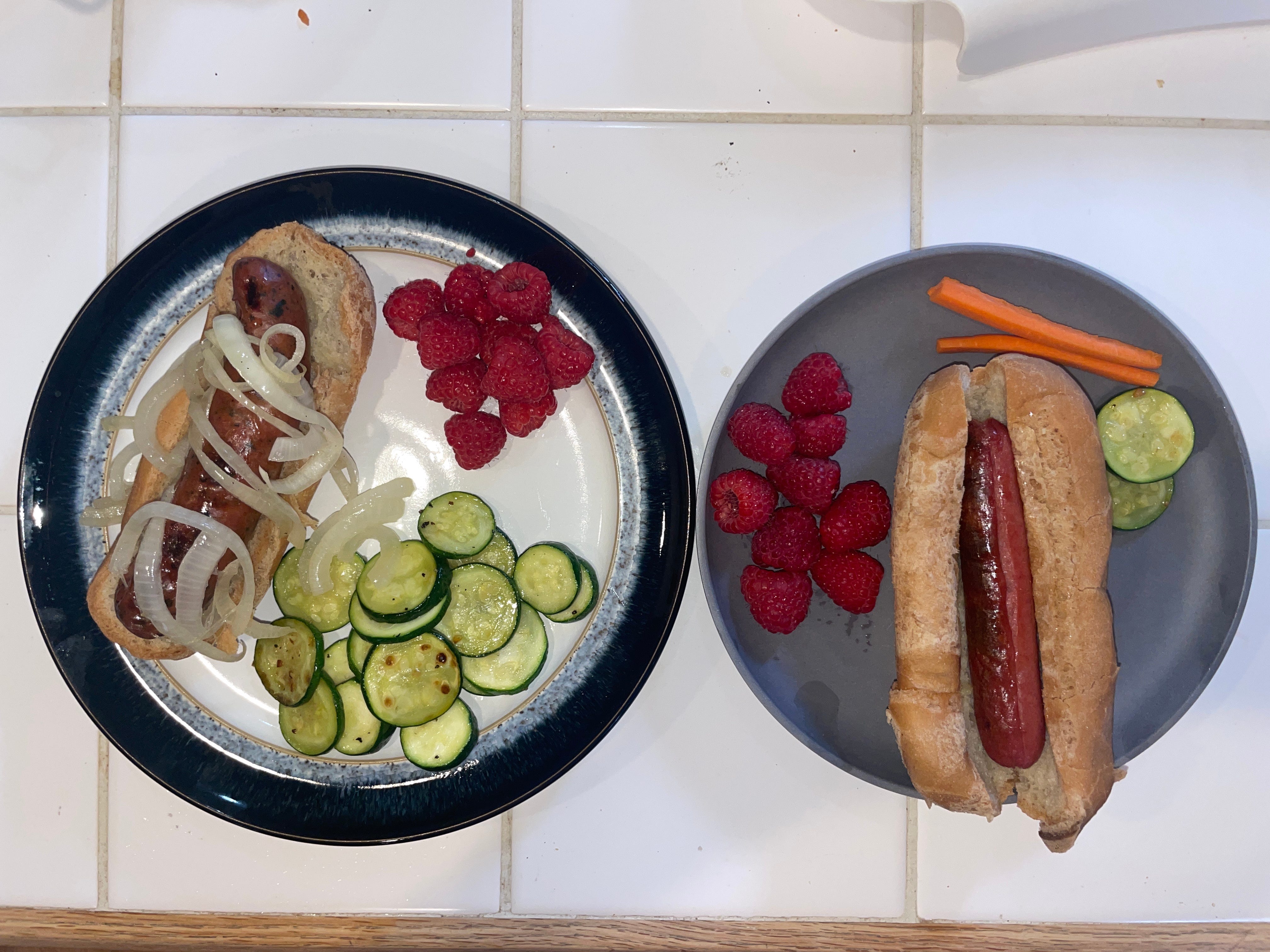 Two plates with hot dogs and veggies on them