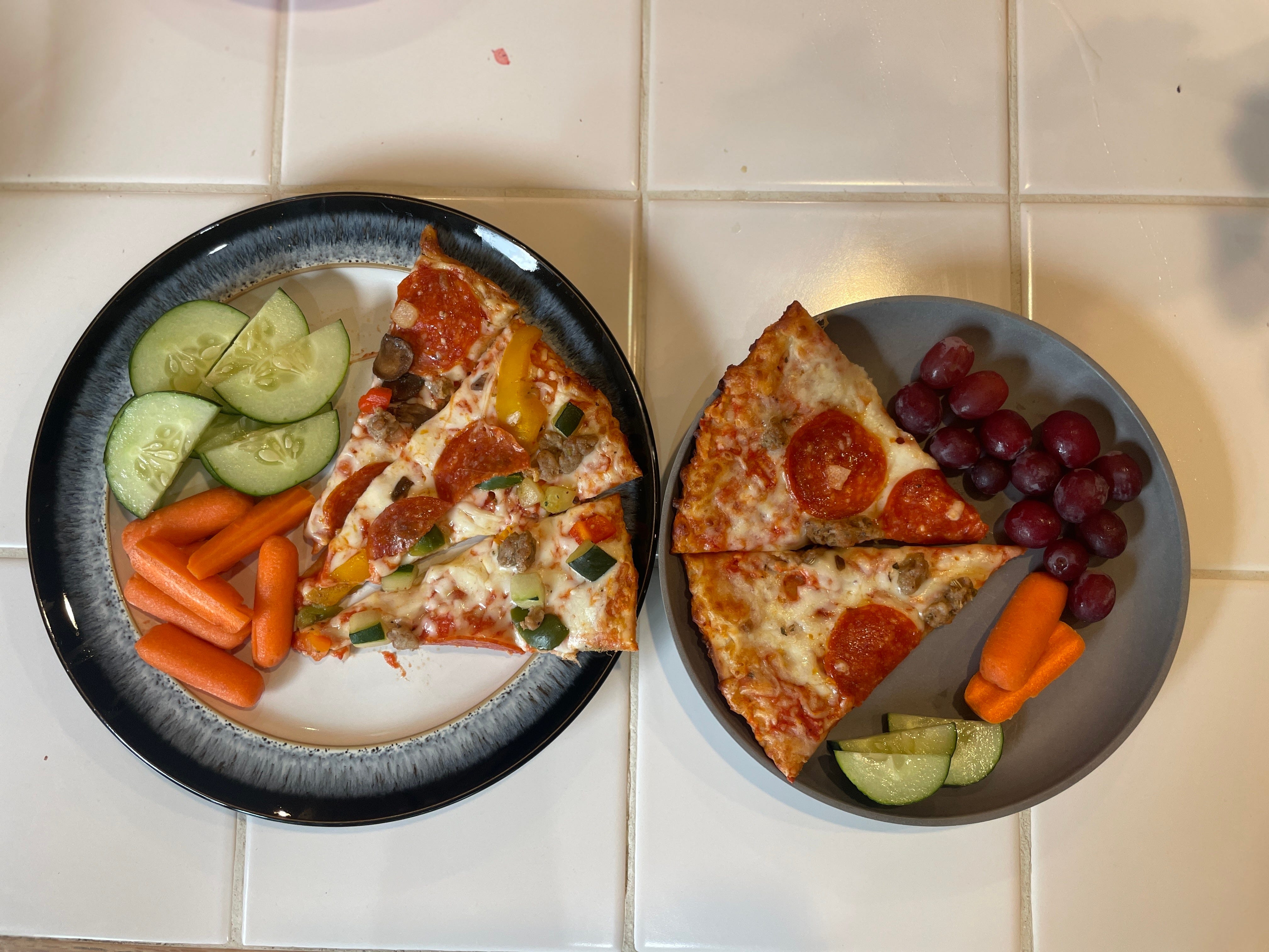 One plate with pizza slices and veggies and one plate with pizza and fruit, veggies