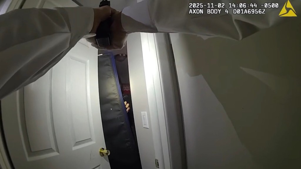 Bodycam footage shows a law enforcement officer holding a pistol and shining a light into a darkened room.