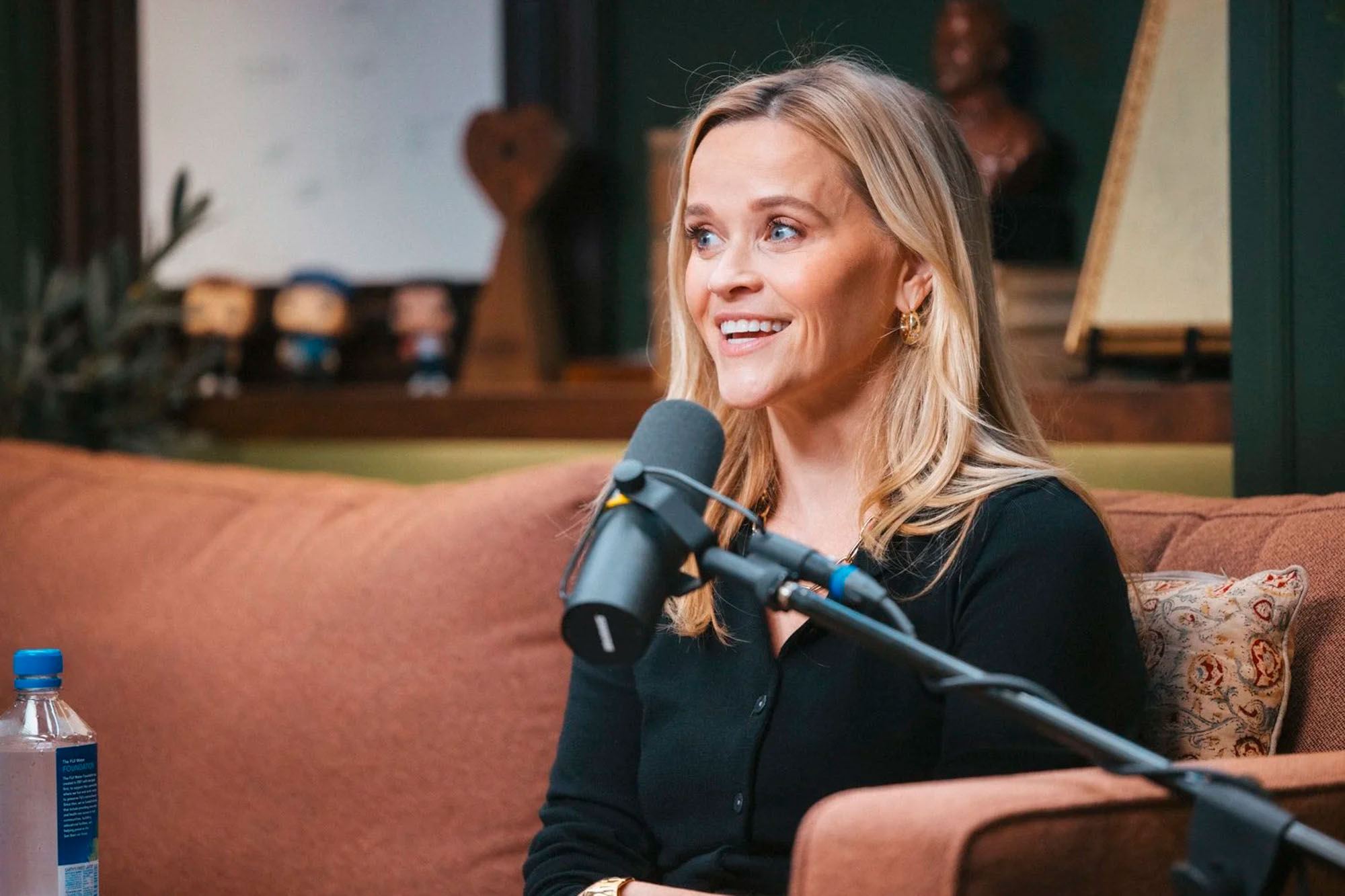 Reese Witherspoon speaking into a microphone on a podcast.