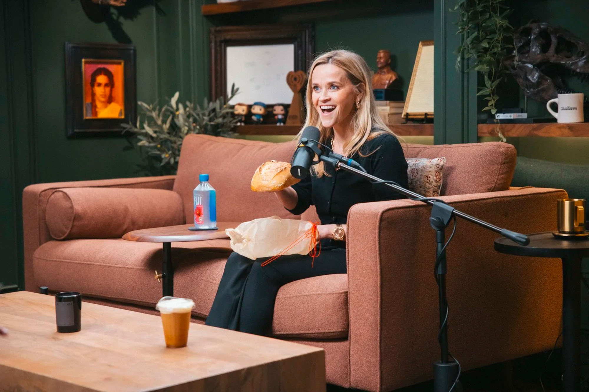 Reese Witherspoon holding a loaf of bread and speaking into a microphone.