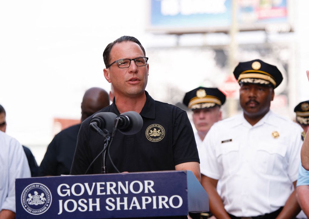 Pennsylvania Governor Josh Shapiro speaks from a podium with two microphones, flanked by other officials.