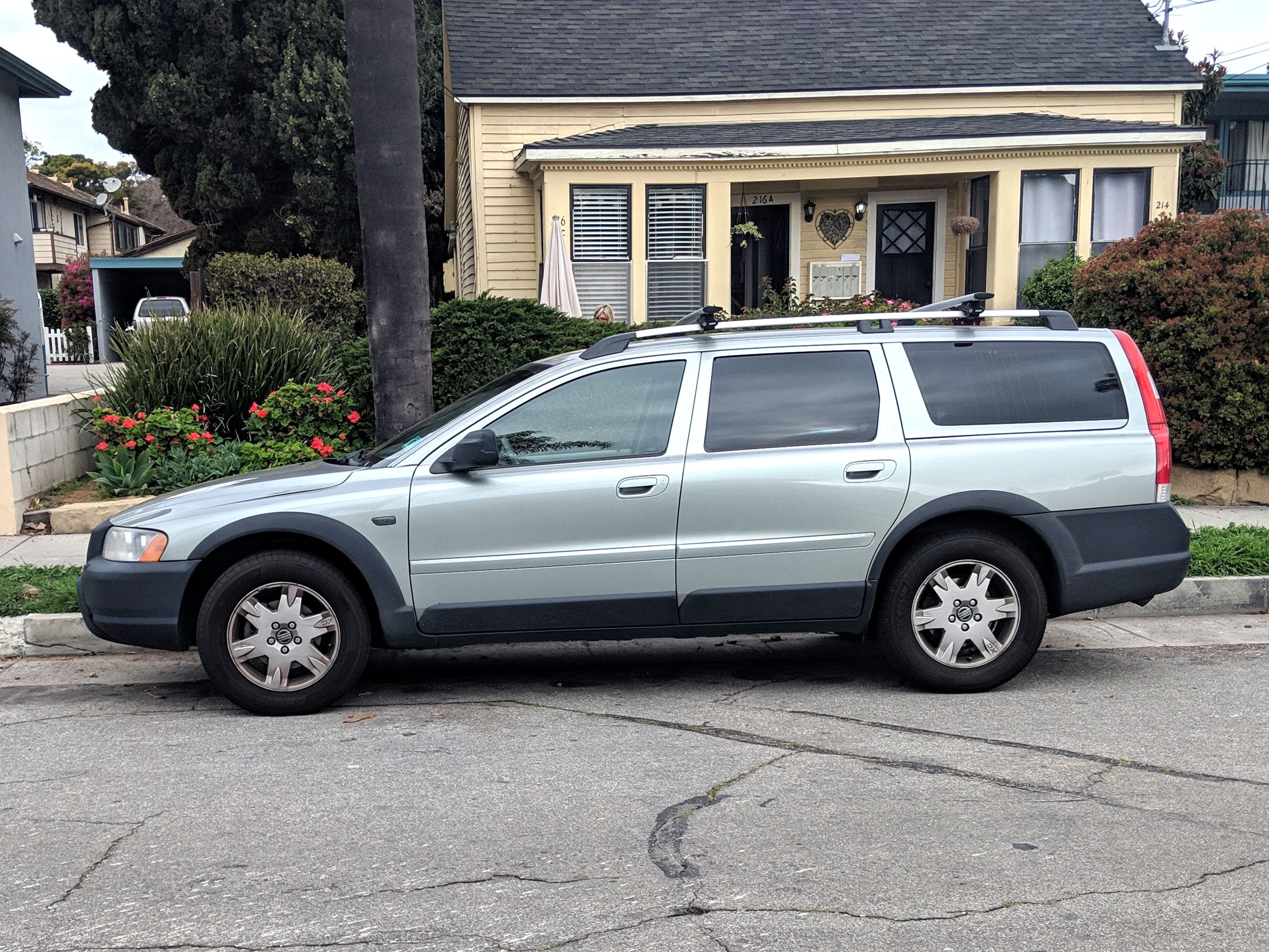 A silver Volvo parked outside a yellow house.