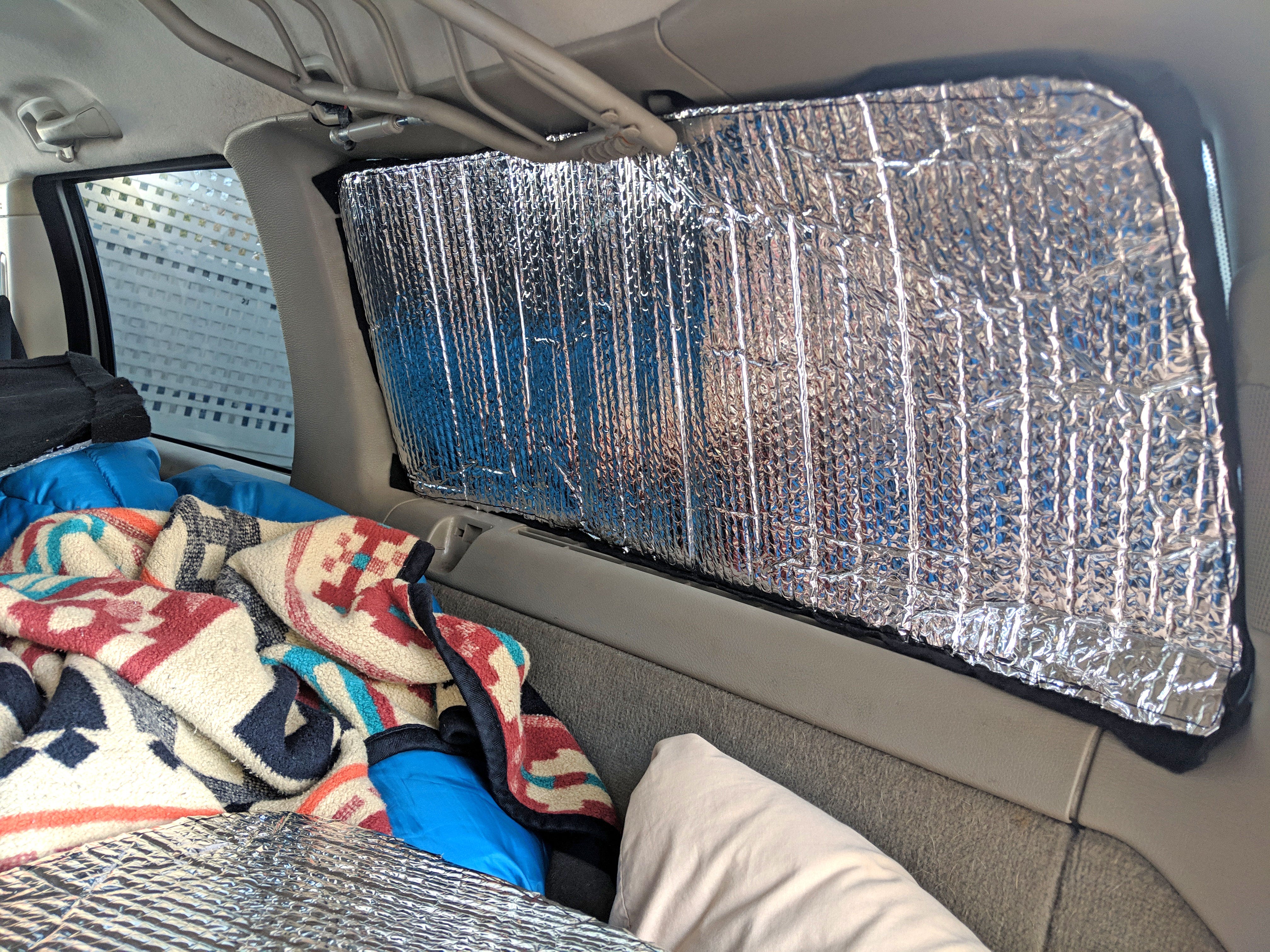 A windshield cover in the window of a car, with blankets piled on the floor.