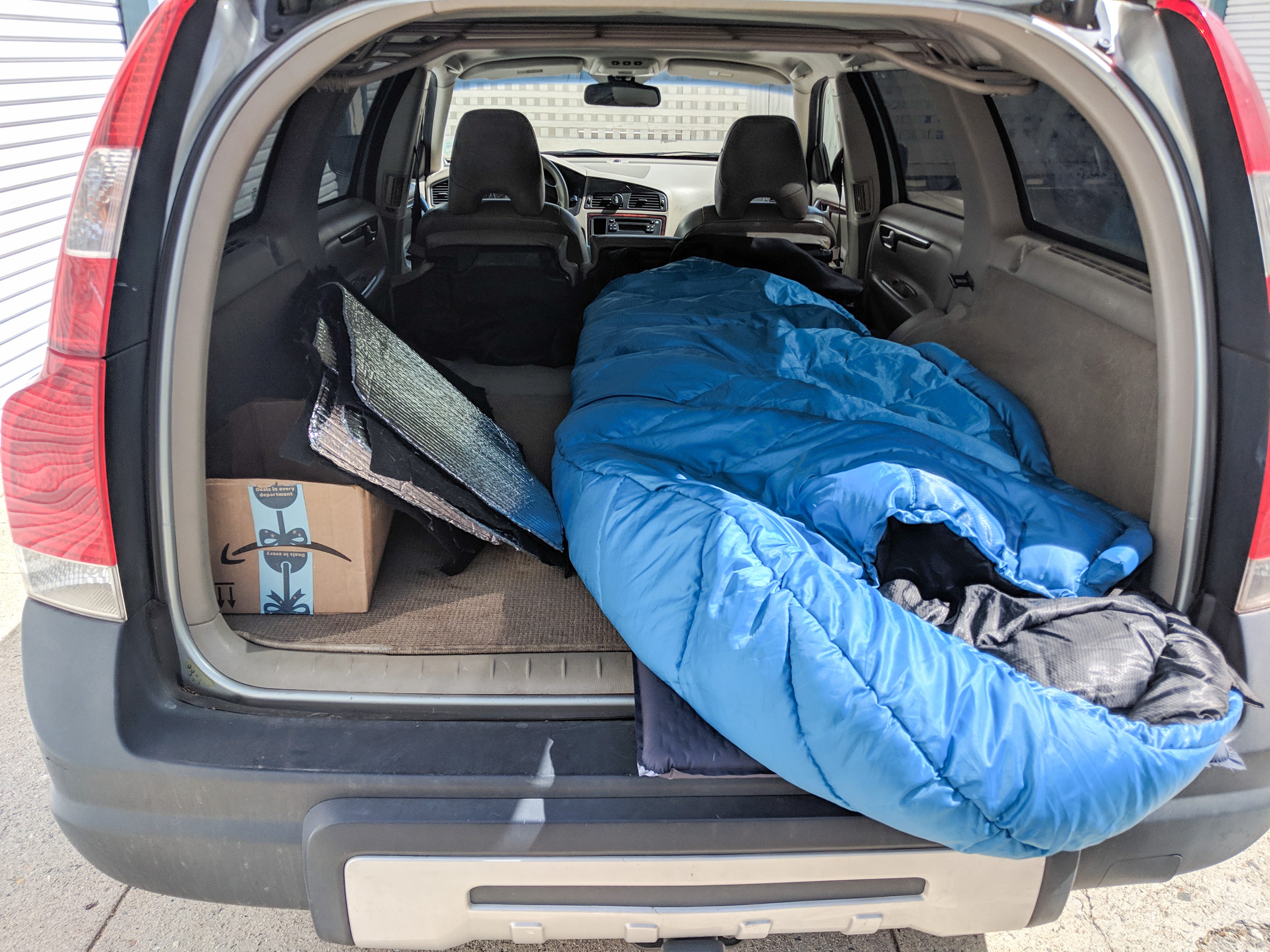 A large blue sleeping bag, a windshield cover, and an Amazon box in the back on a car with the seats folded down.