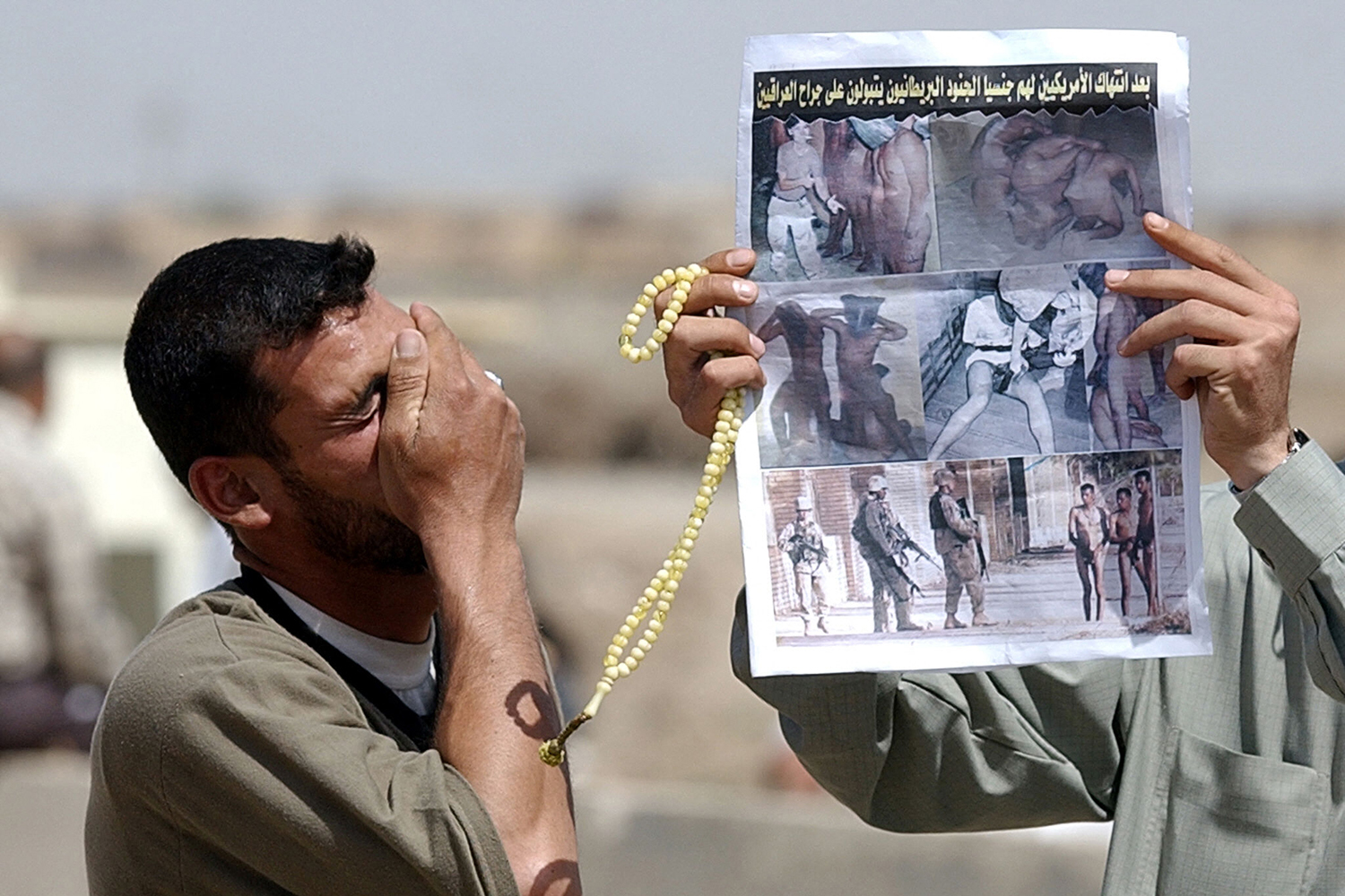 A man holds his hand to his face while another holds up a newspaper.