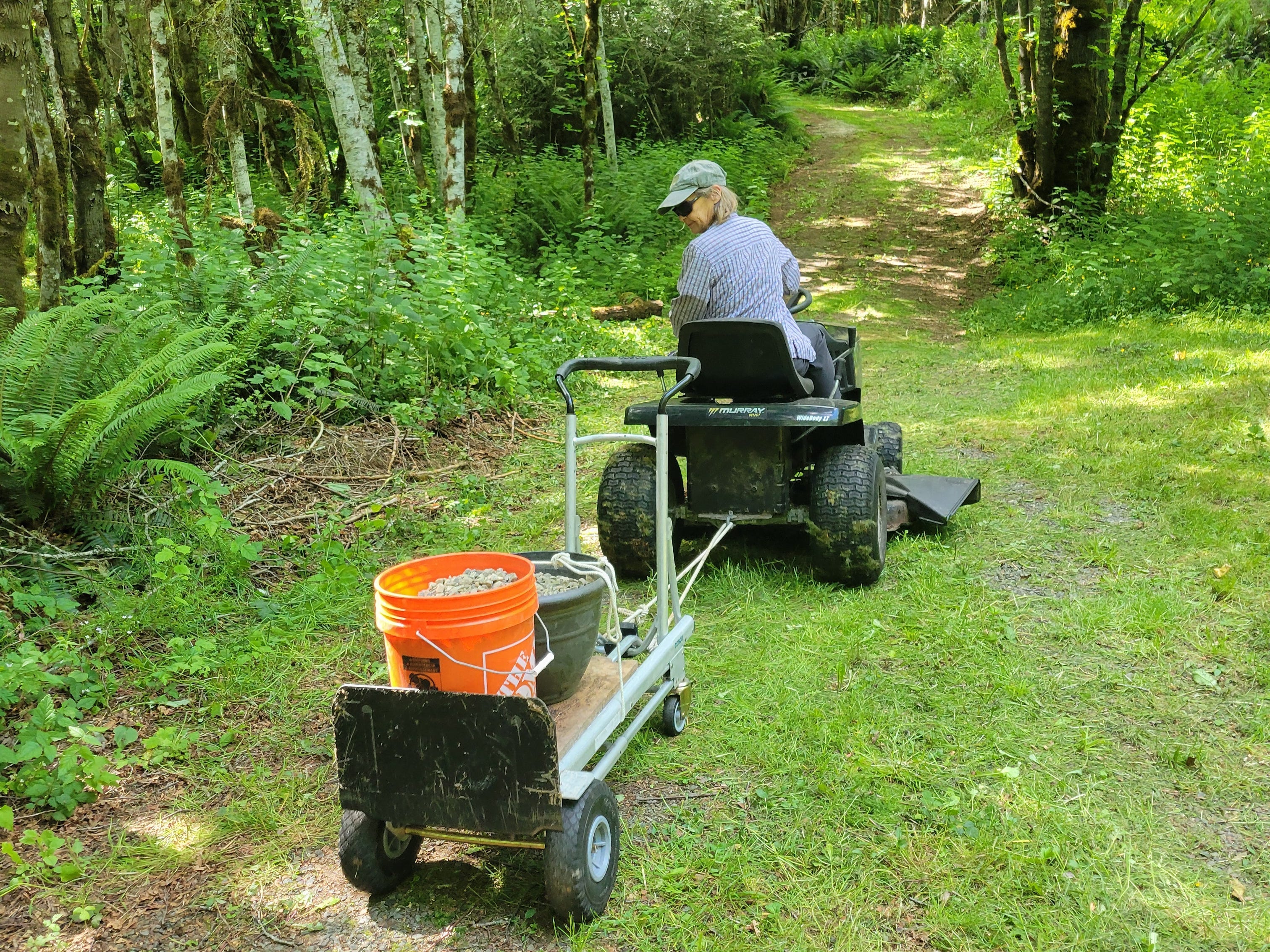 Woman driving lawnmower, pulling water on wheeled cart