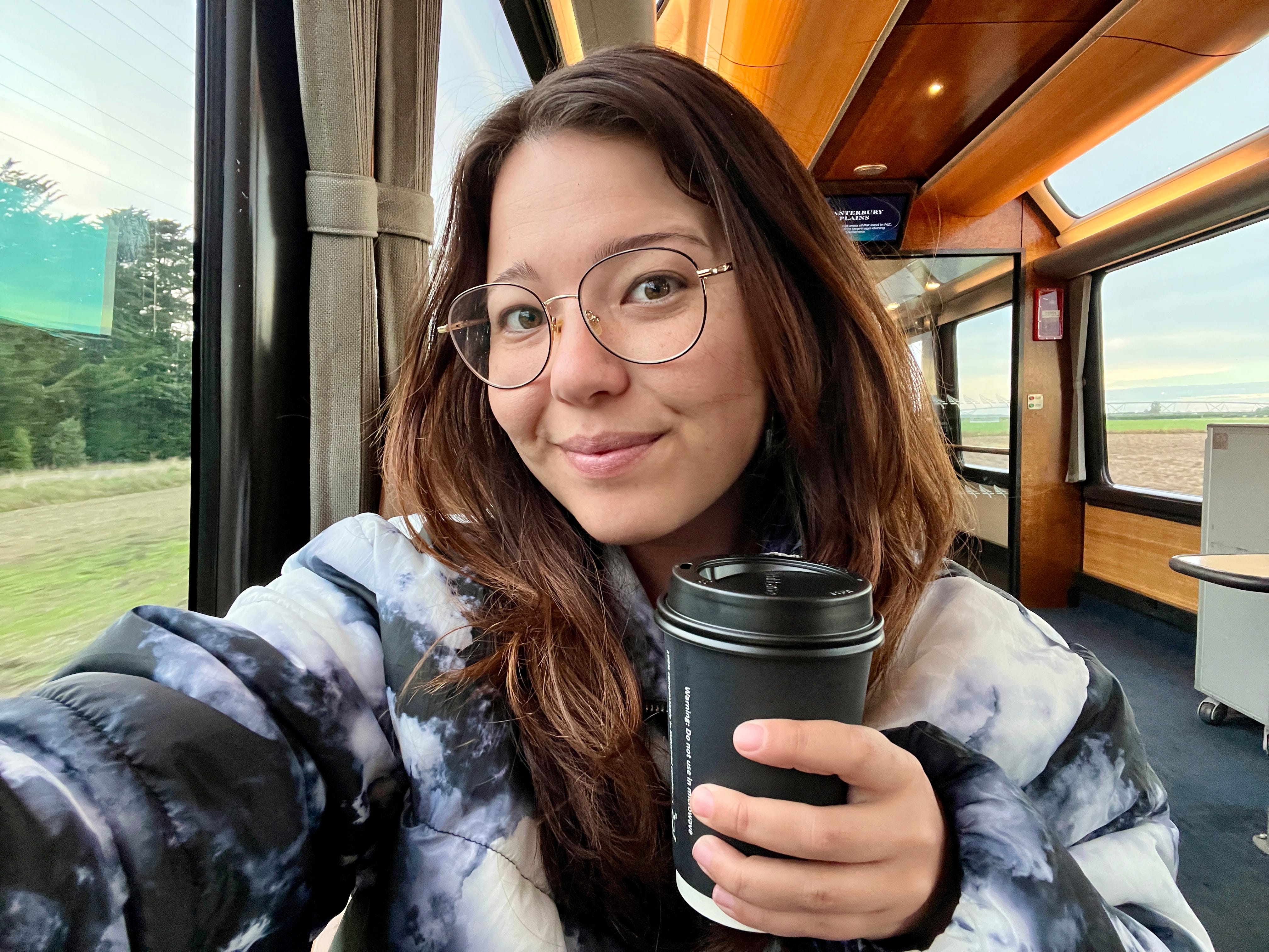 Author Ashley Probst smiling with coffee cup on TranzAlpine train