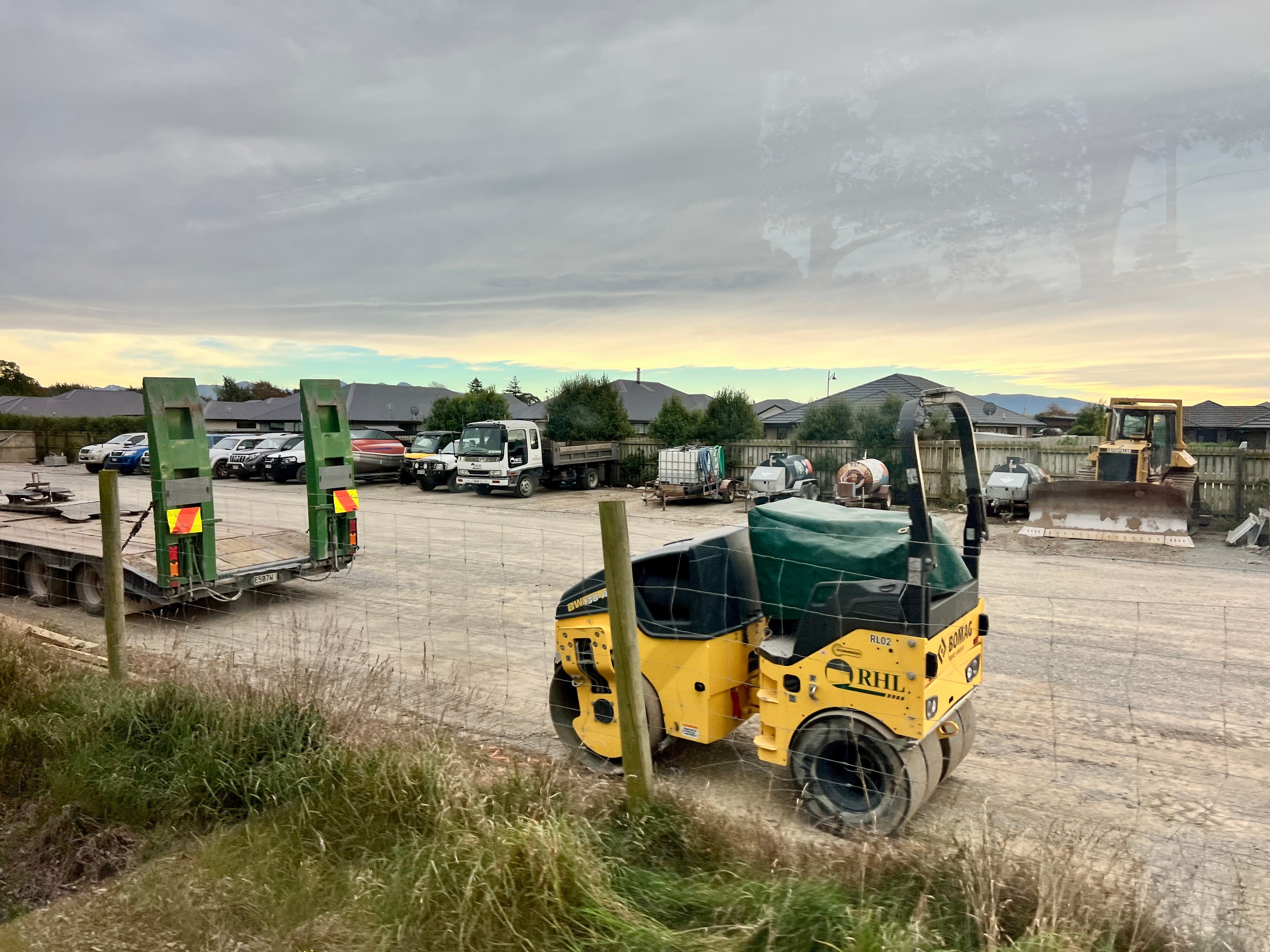View of construction vehicles, trucks in dirt lot from window