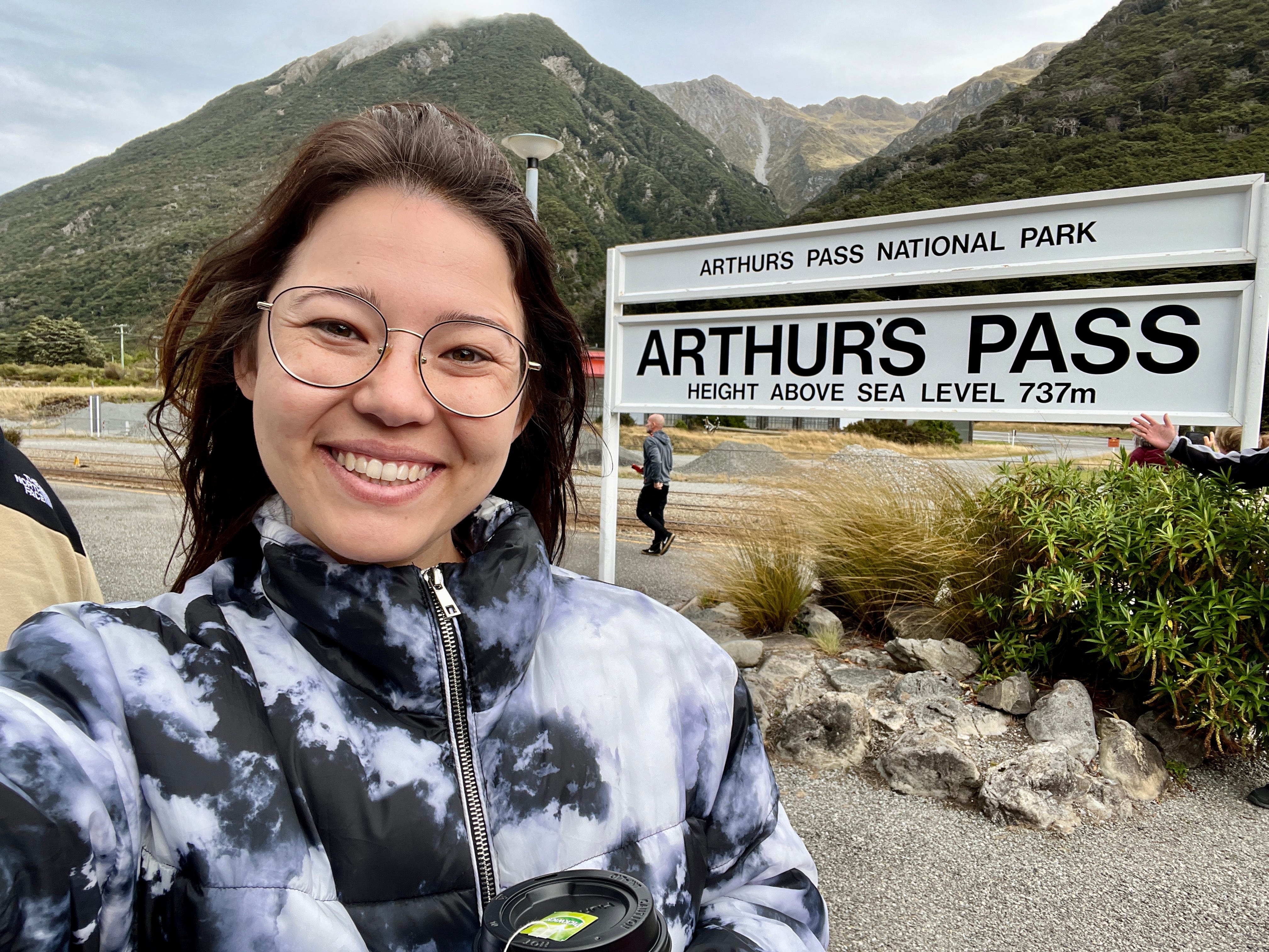 Author Ashley Probst smiling next to sign for Arthurs Pass National Park