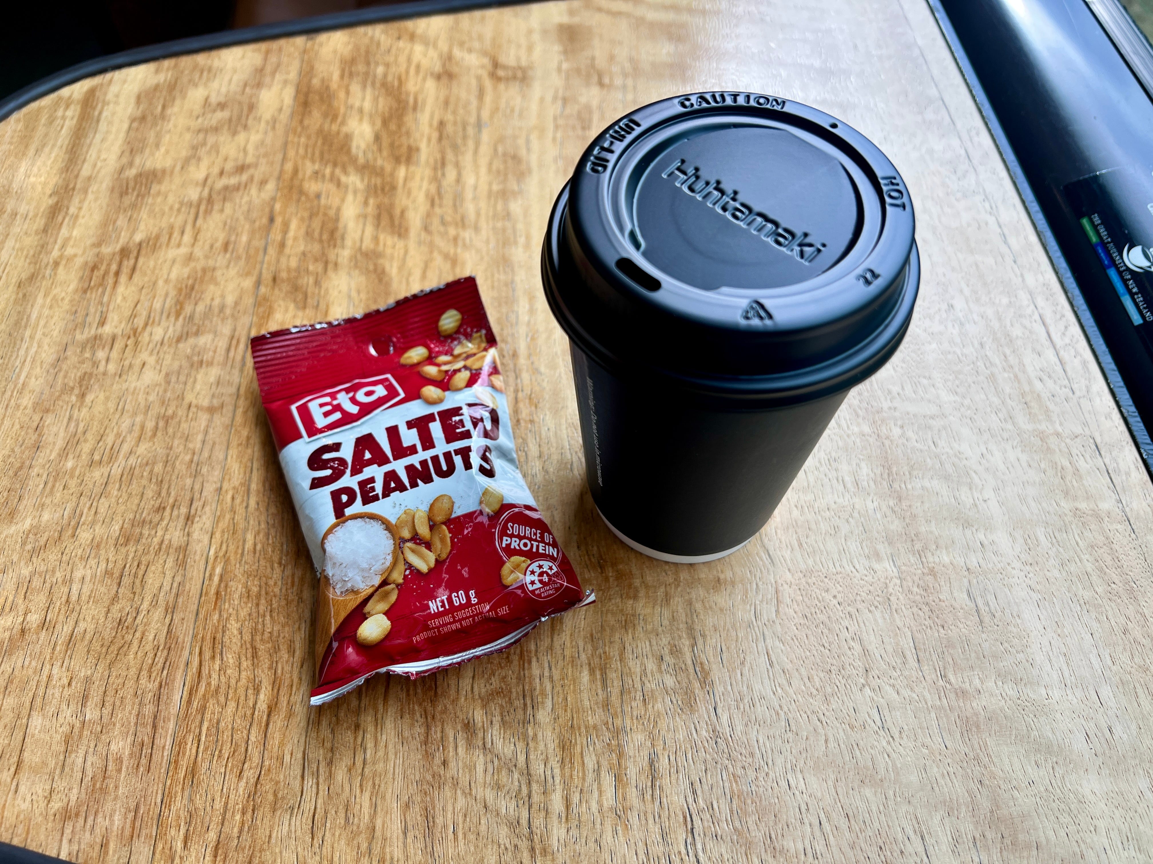 Coffee cup next to ETA bag of salted peanuts on train tray table
