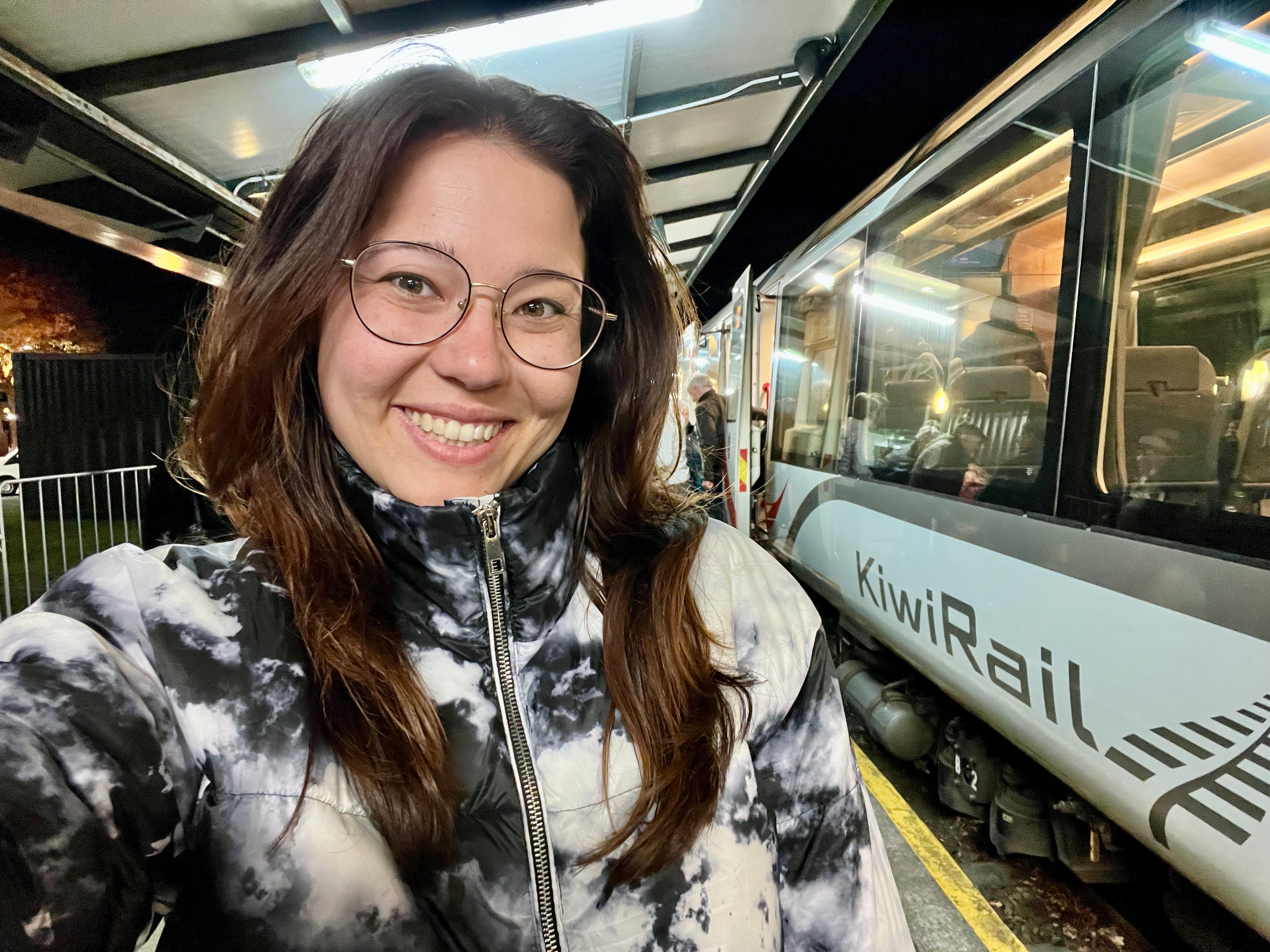 Author Ashley Probst smiling next to Kiwi Rail train at night
