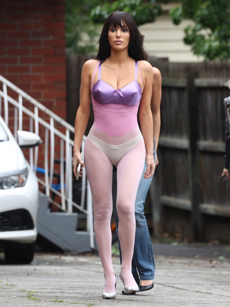 Bianca Censori in a lilac bodysuit with pink tights and white heels.