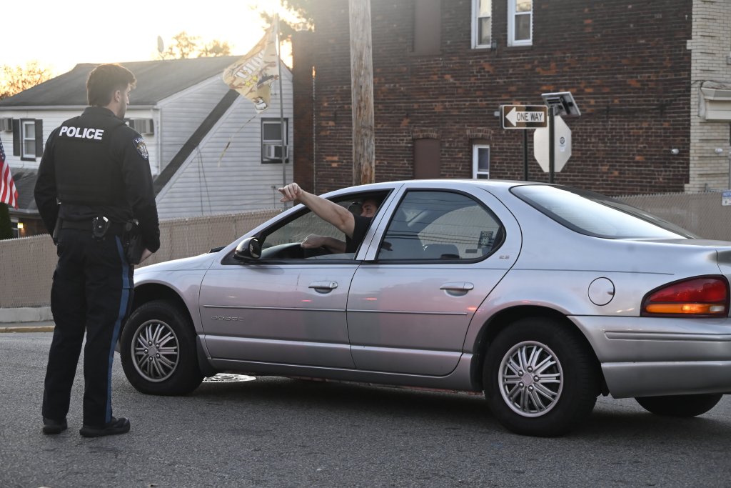 A police officer speaking with a man in a silver Dodge car.