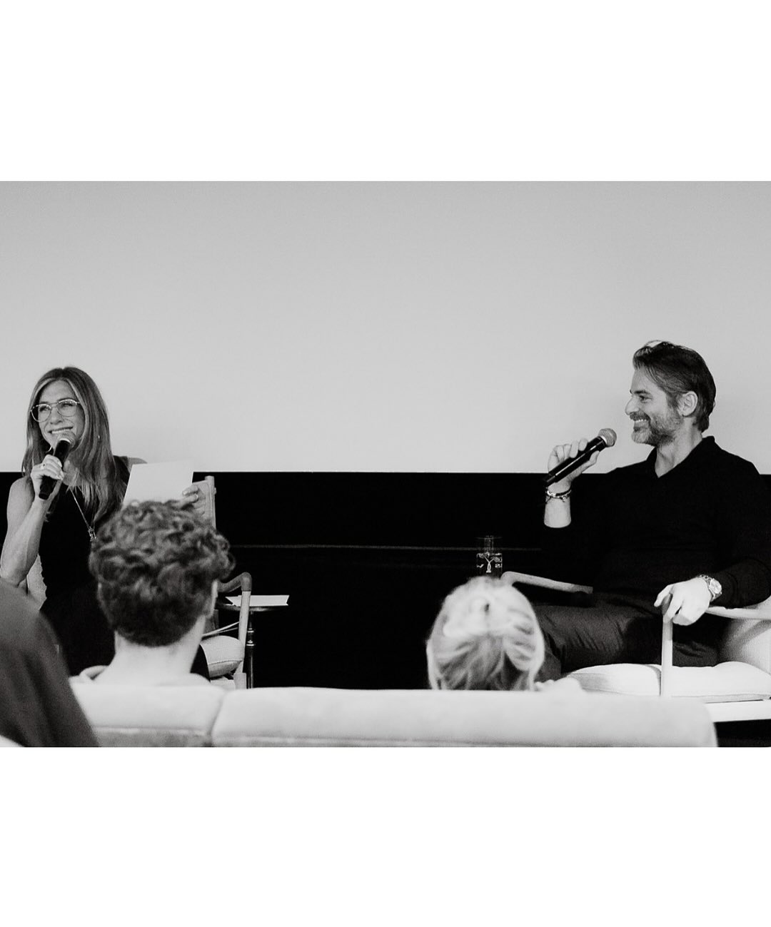 Jennifer Aniston and Jim Curtis on stage talking into microphones.