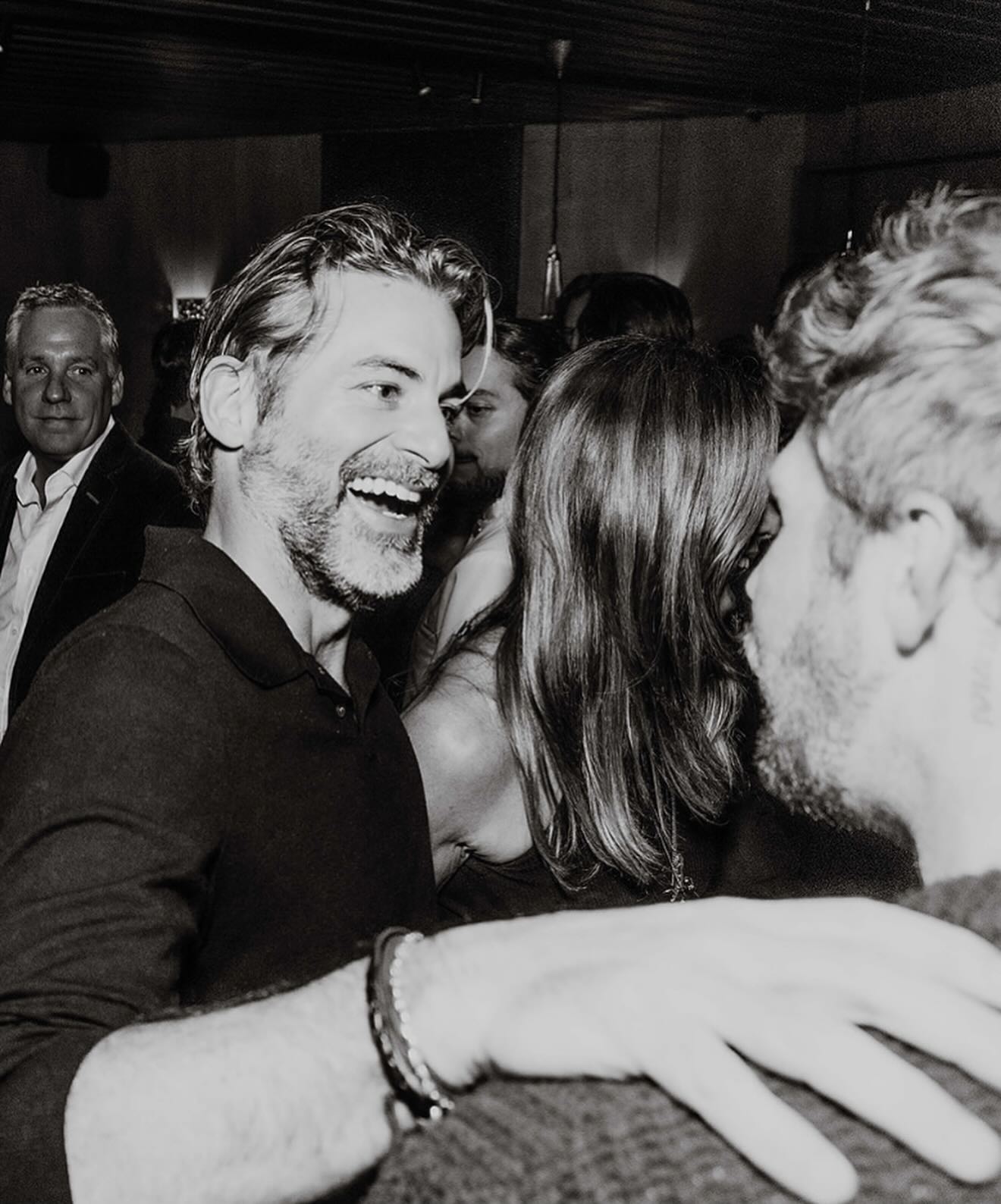 Black and white photo of a man smiling and another person with their back to the camera.