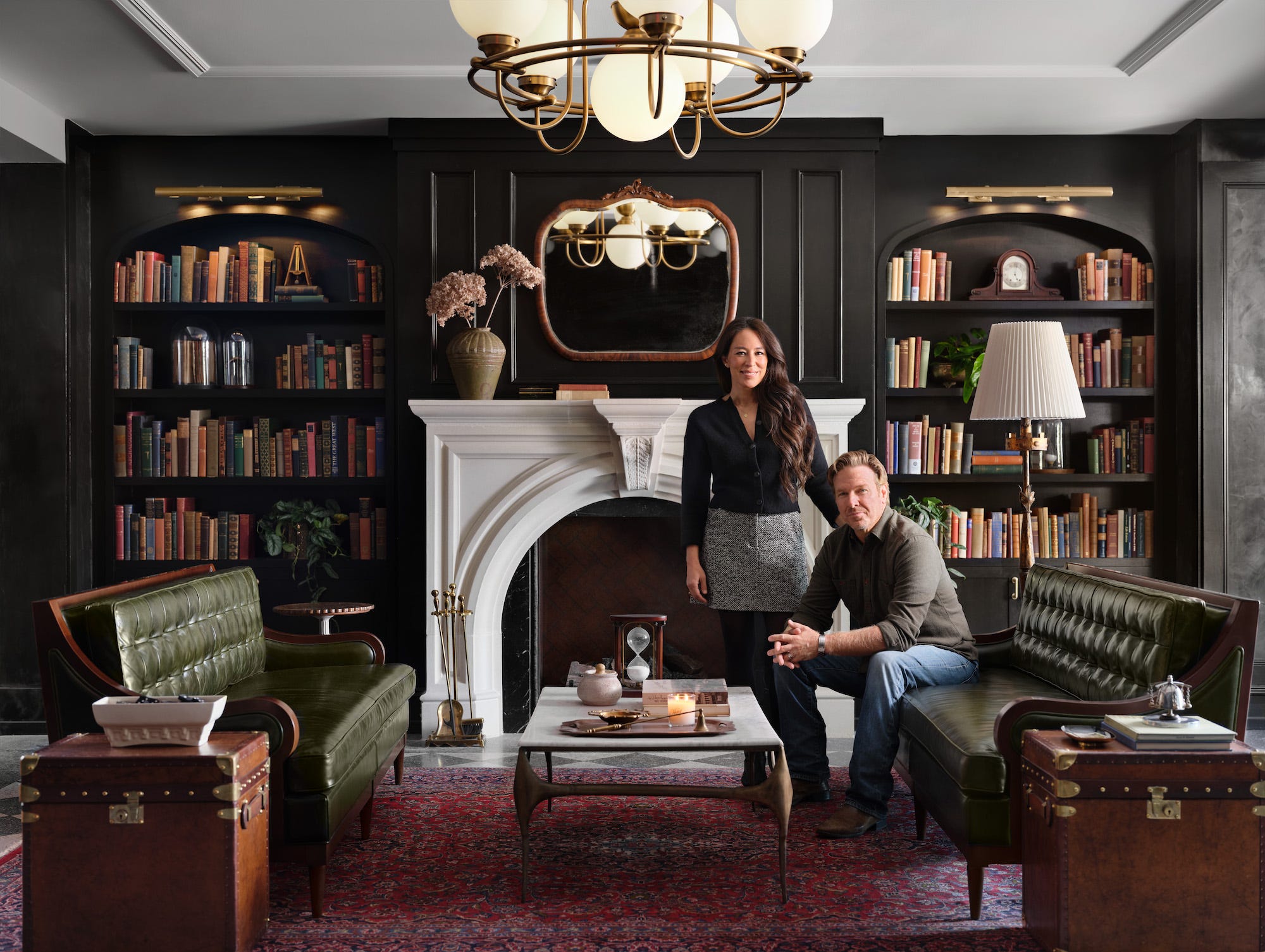 Chip and Joanna Gaines pose in a library with built-in bookshelves and a white fireplace.