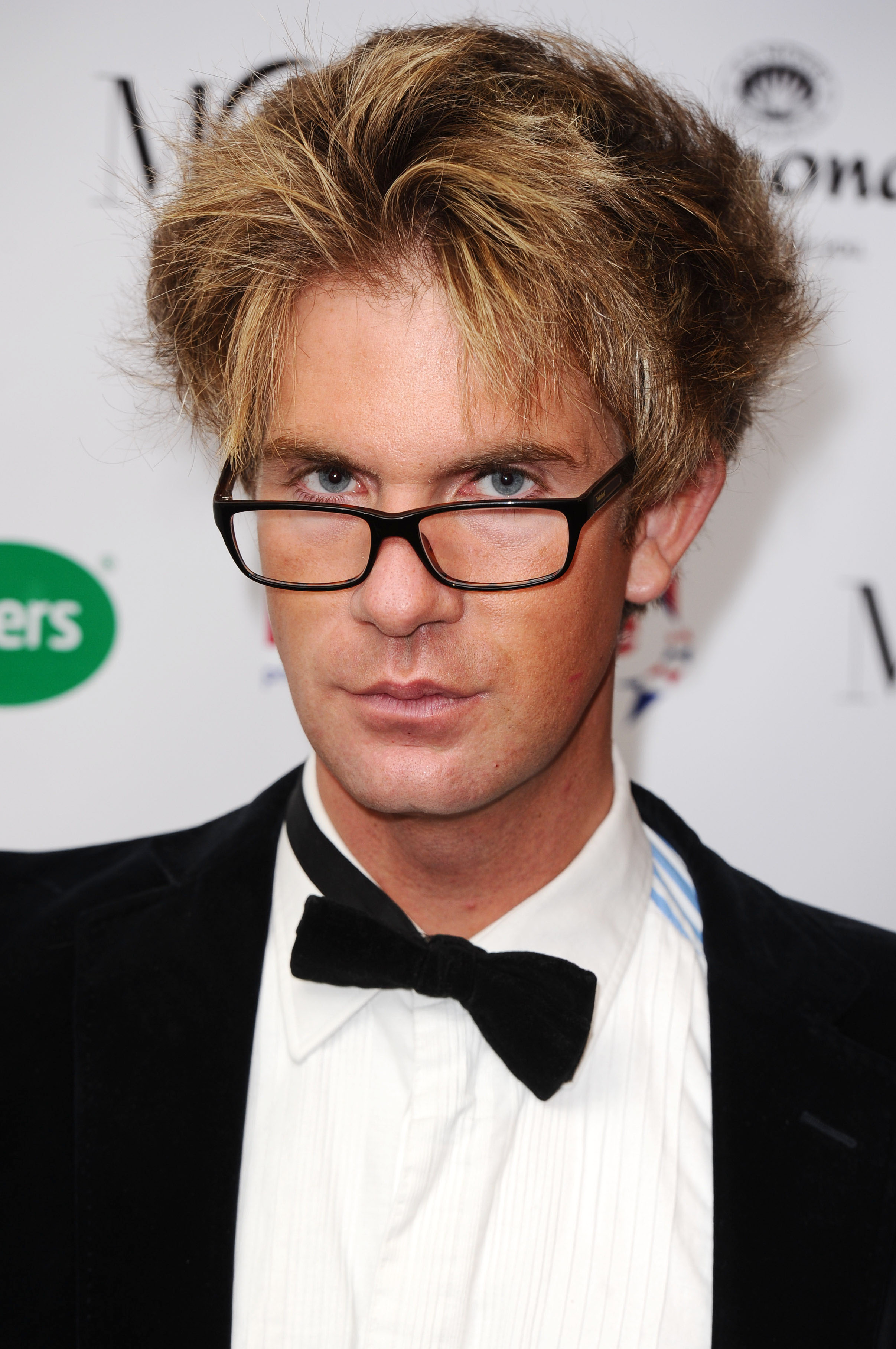 Headshot of Ben Duncan with messy blond hair, wearing glasses, a white dress shirt, and a black velvet bow tie.