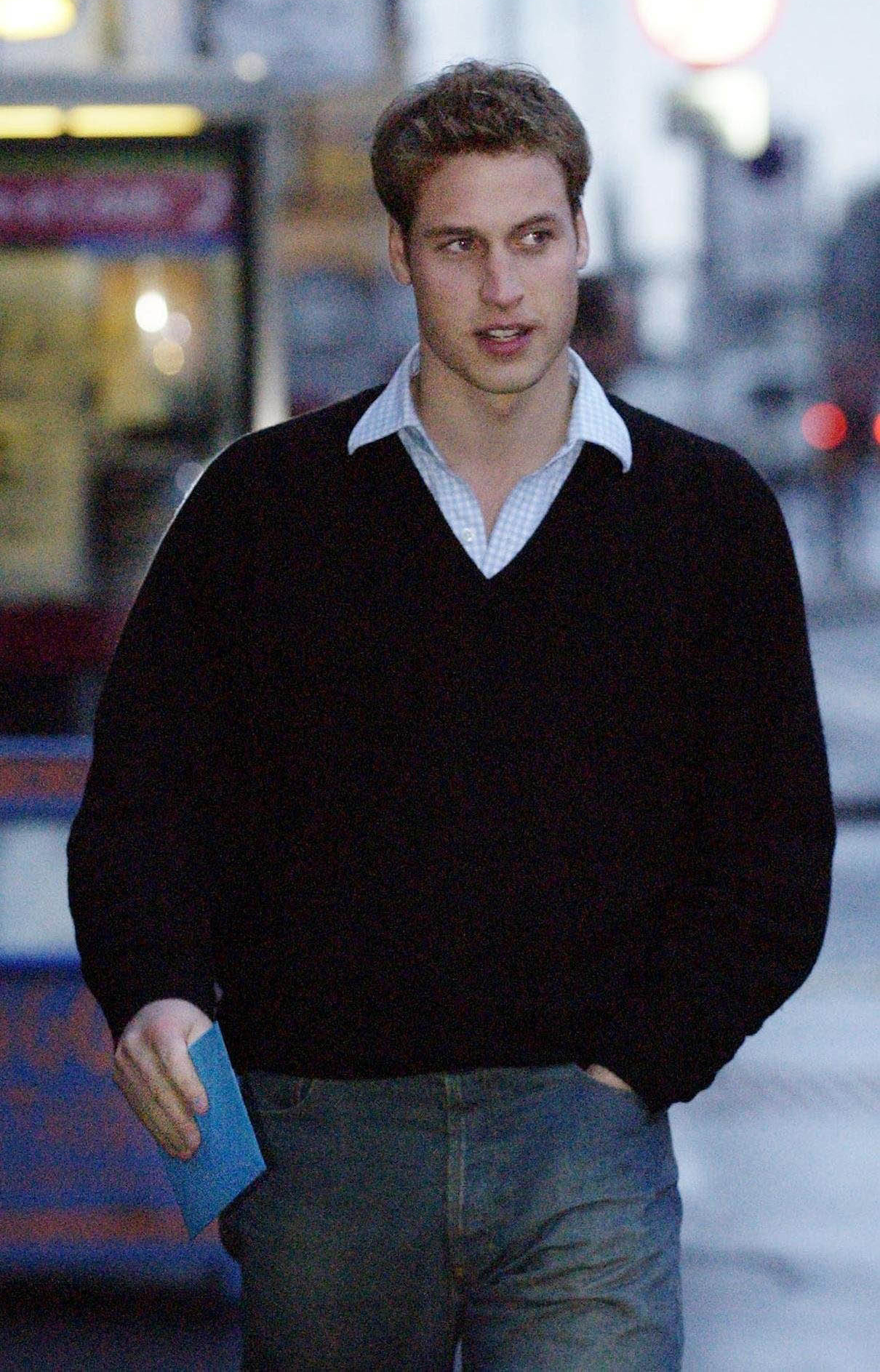 Prince William wearing a black sweater over a light blue checkered shirt, with jeans.