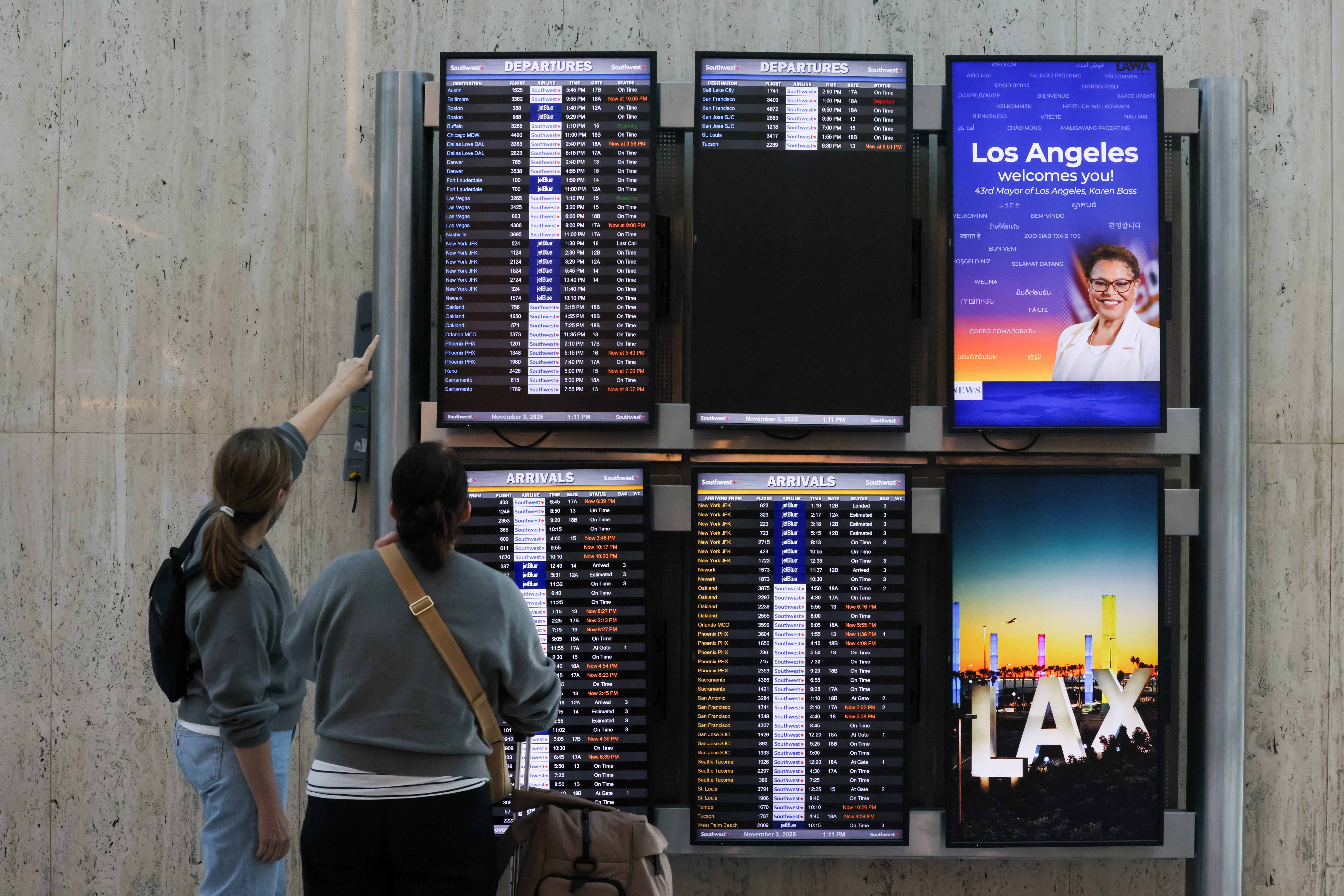 Passengers at LAX looking a flight departures board.