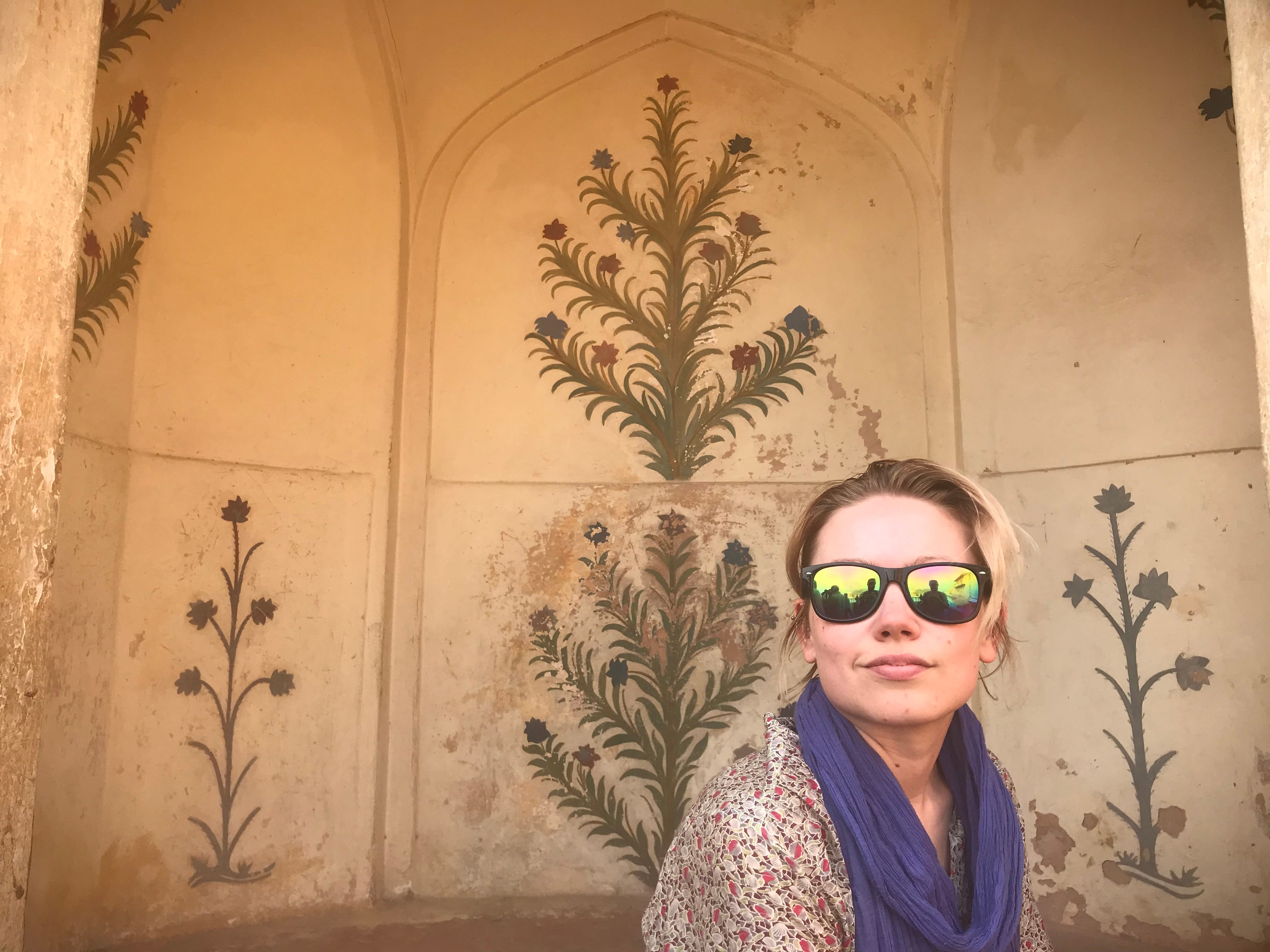 The author in front of a wall with floral patterns.
