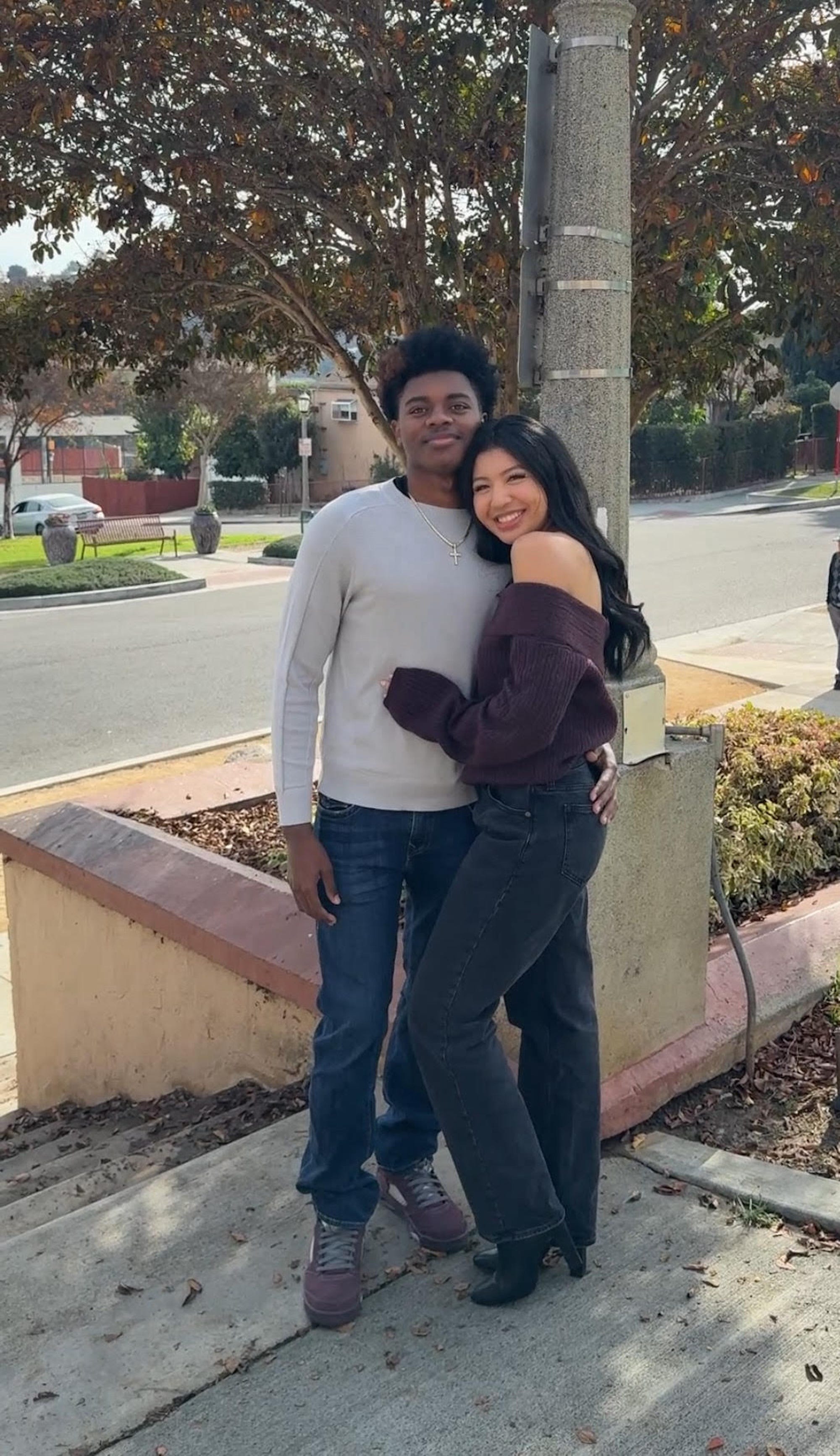 A couple stands together in front of a staircase, embracing.