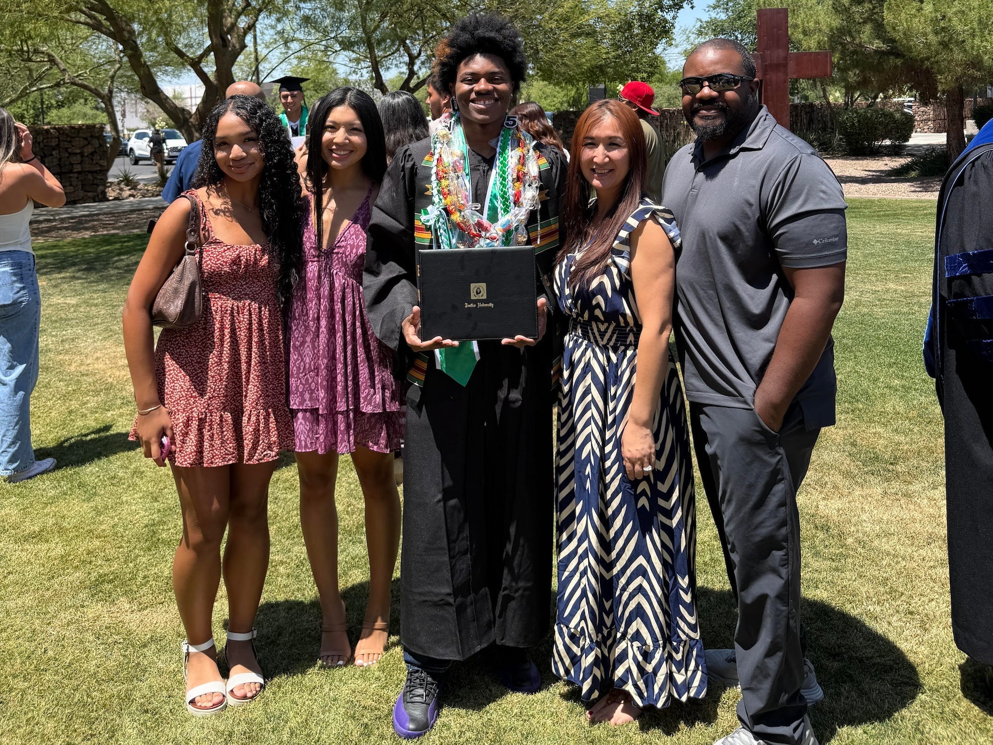 Four people stand with a graduate in a lawn.