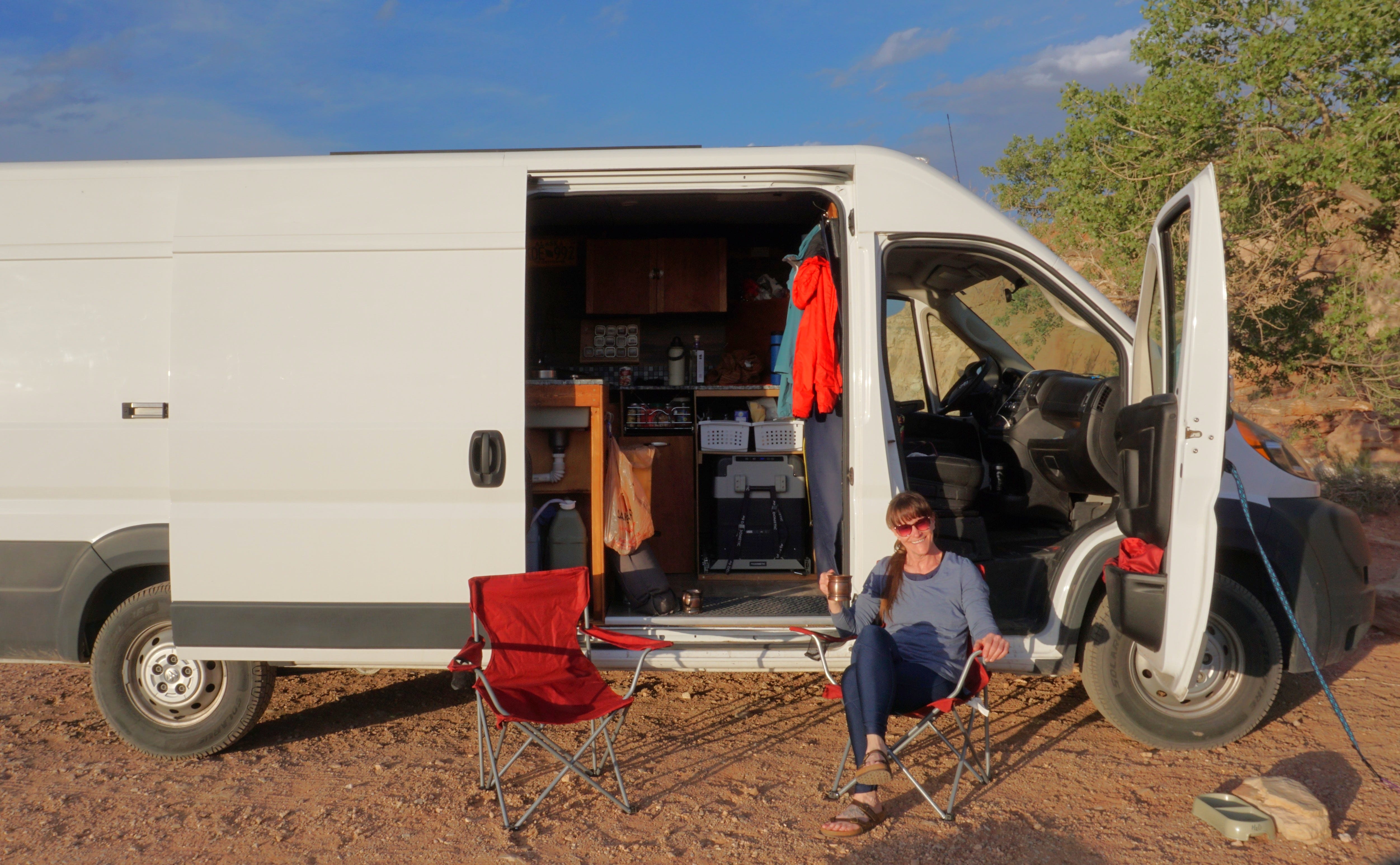 Woman sitting on chair outside of camper with open doors