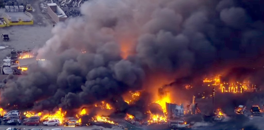 Aerial view of a large fire with thick black smoke engulfing a Louisville airport facility and surrounding area.