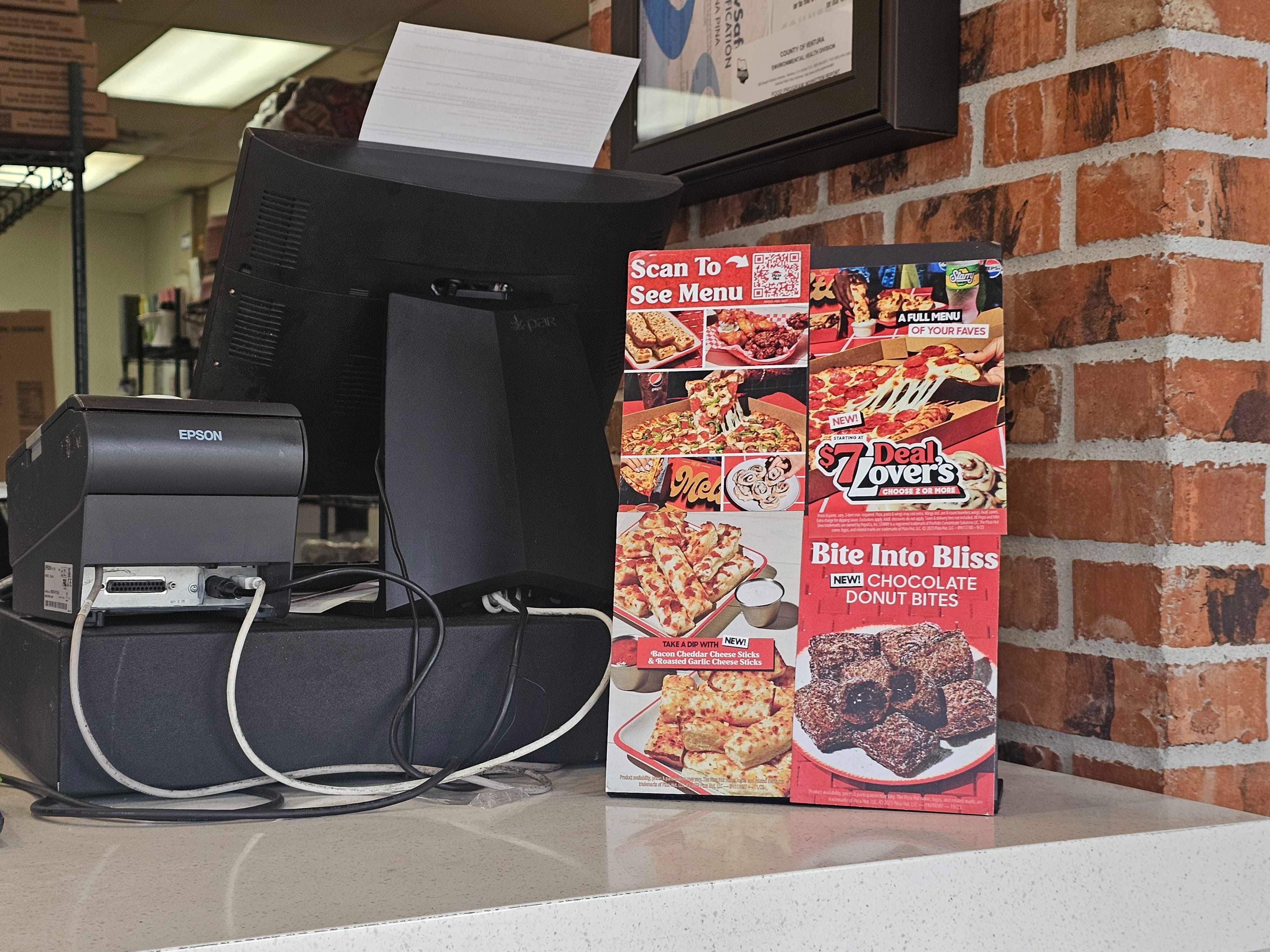Small cardboard pop-up displays at a Pizza Hut cash register show a scannable QR code to view the menu.