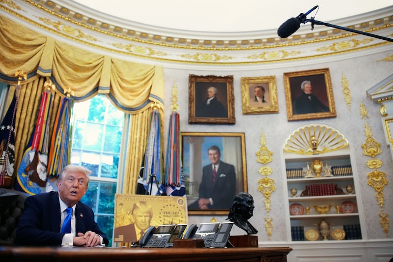 President Donald Trump delivers remarks alongside a poster of the "Trump Gold Card" in the gold-covered Oval Office.