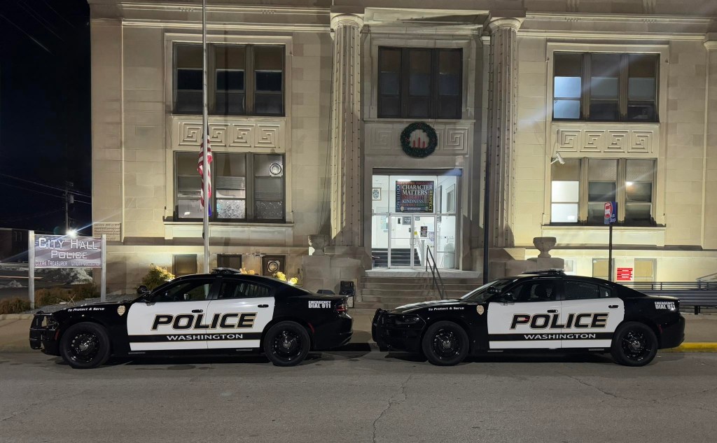 Two police cars parked outside the Washington City Hall building at night.