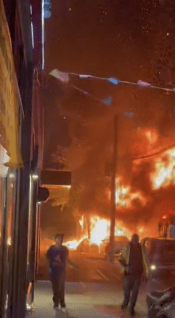 A building engulfed in flames with people running away.