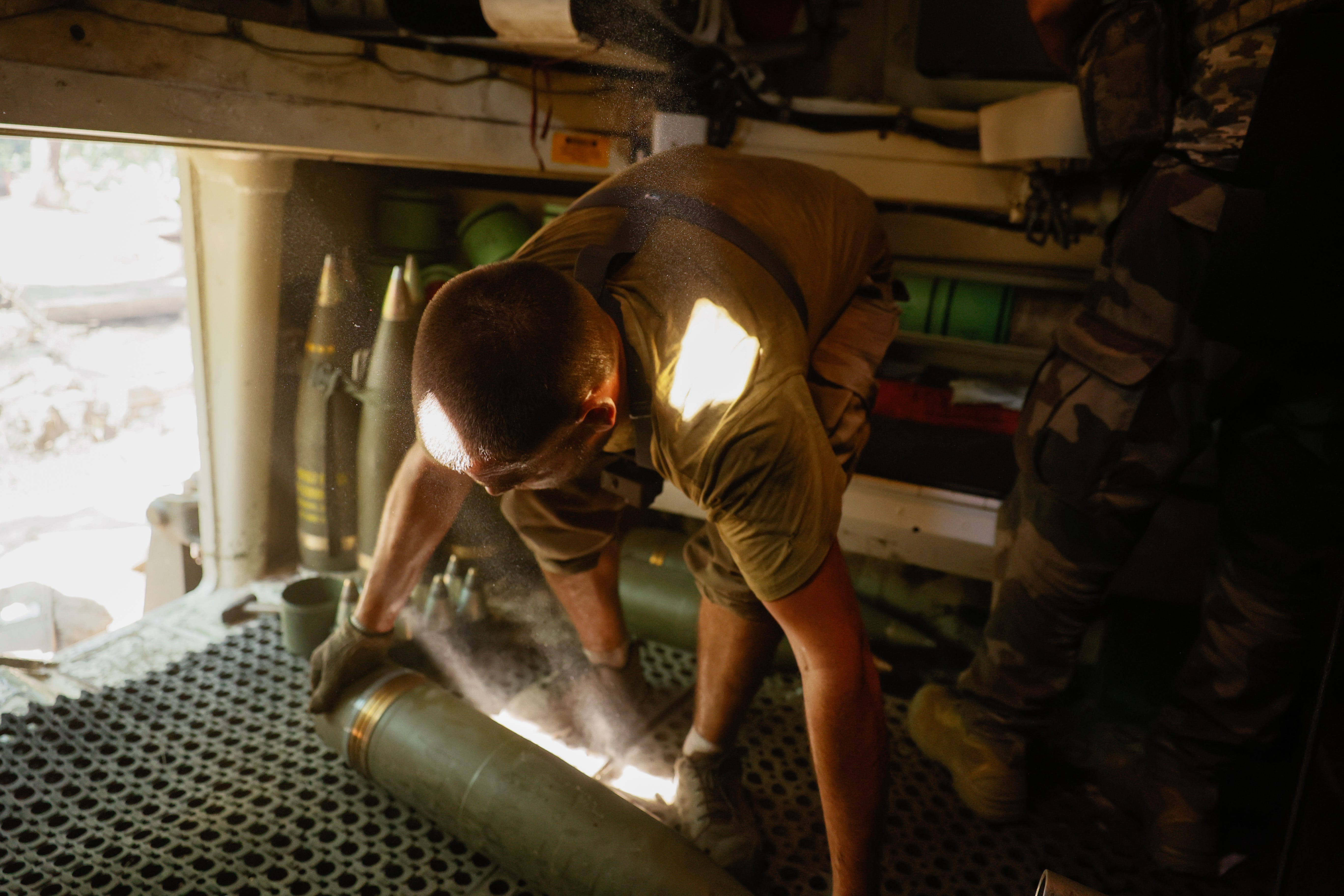 A Ukrainian serviceman picks up a 155mm artillery shell.