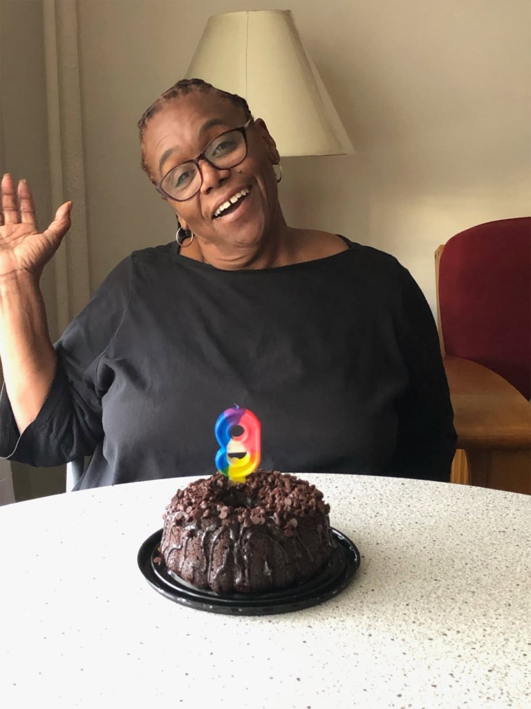 Theresa Stukes waving next to a chocolate cake with a number 9 candle.