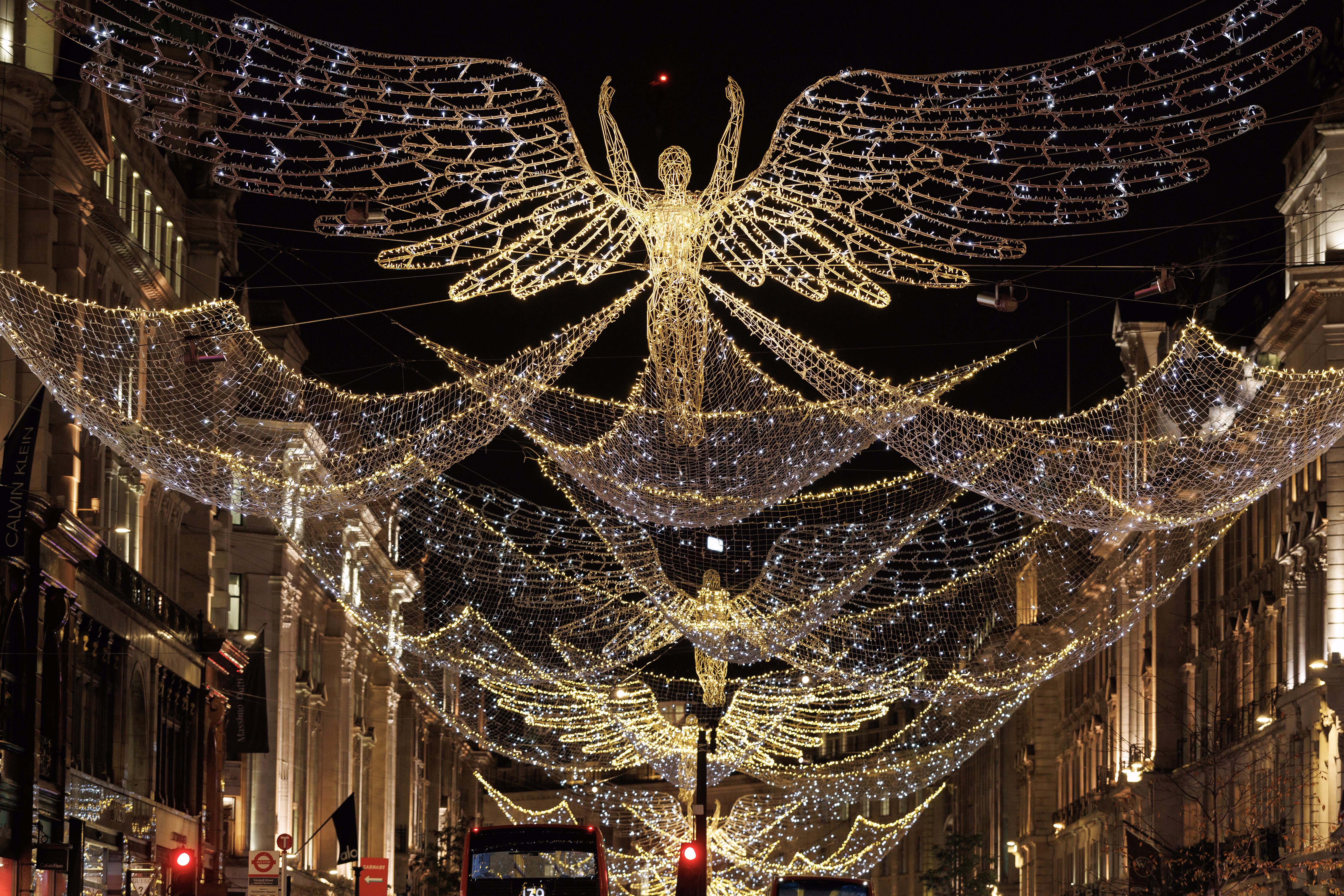 Rows of angel-shaped light sculptures are suspended above a street in a shopping district.