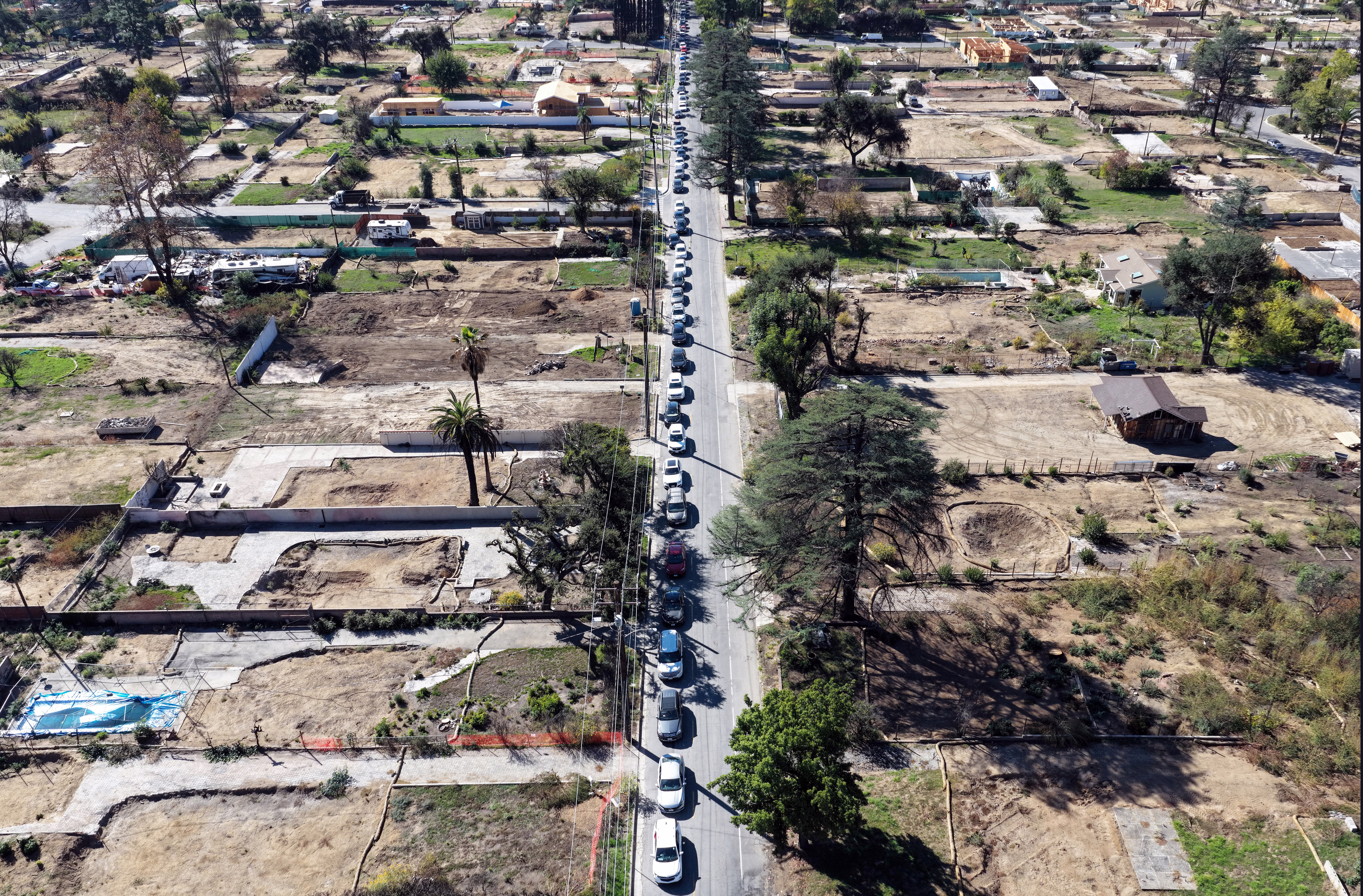 An aerial view of a long line of cars on a street that passes through many empty lots in a residential area affected by a wildfire months ago.