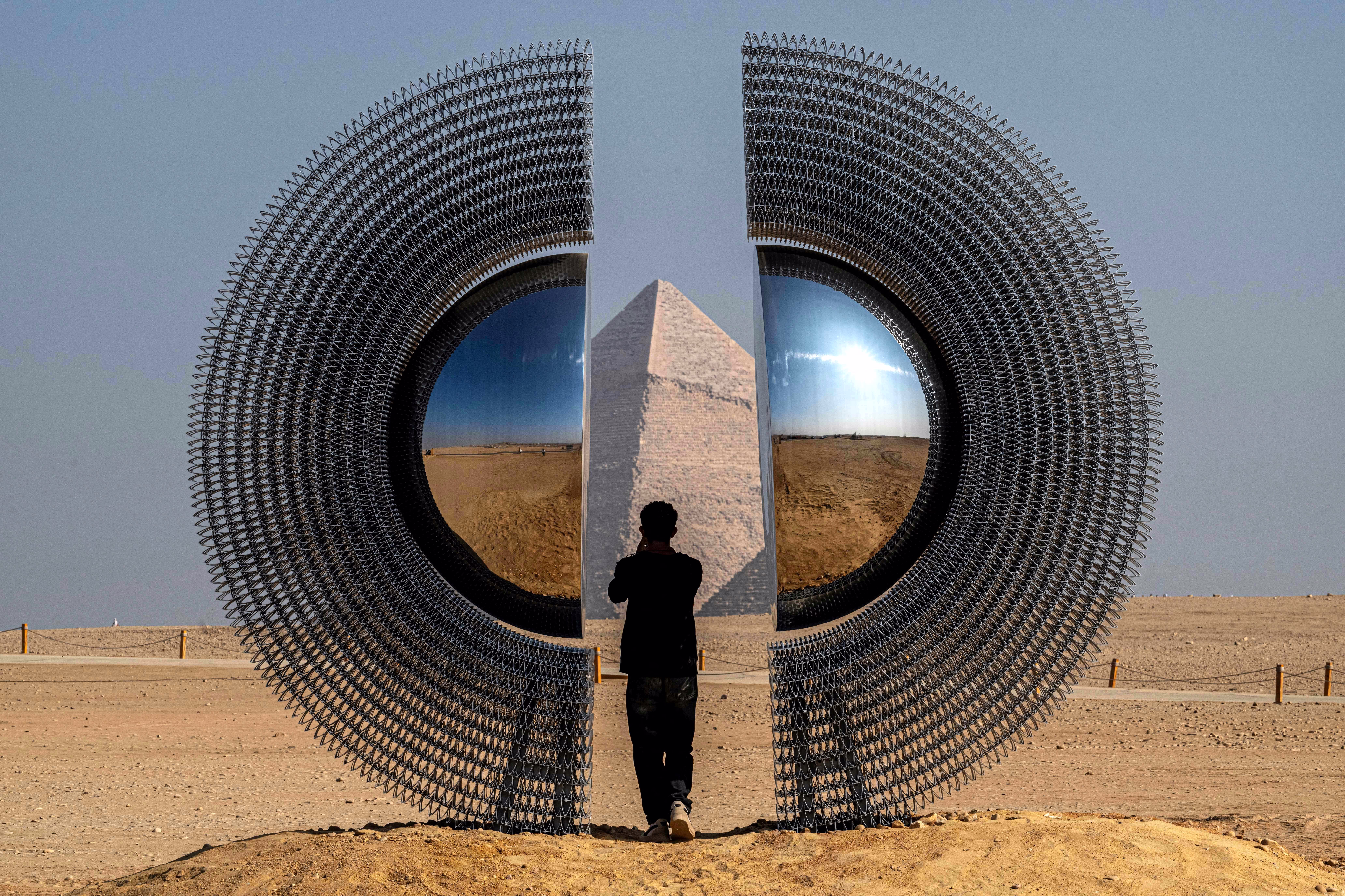 A person stands inside a large circular art installation that has been set up beside the Giza pyramids in Egypt.