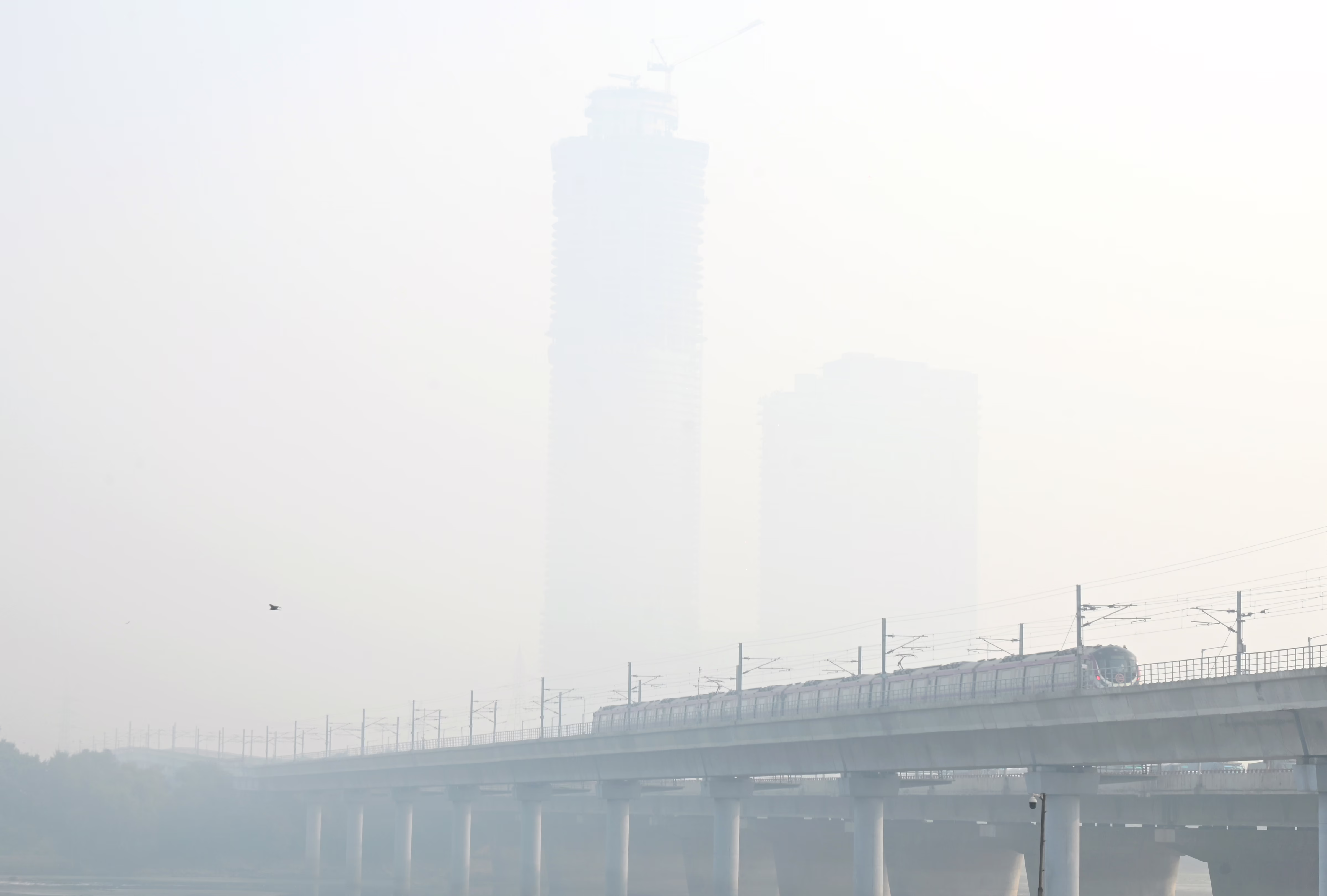 A view of a train passing over a bridge and distant tall buildings on a very smoggy day