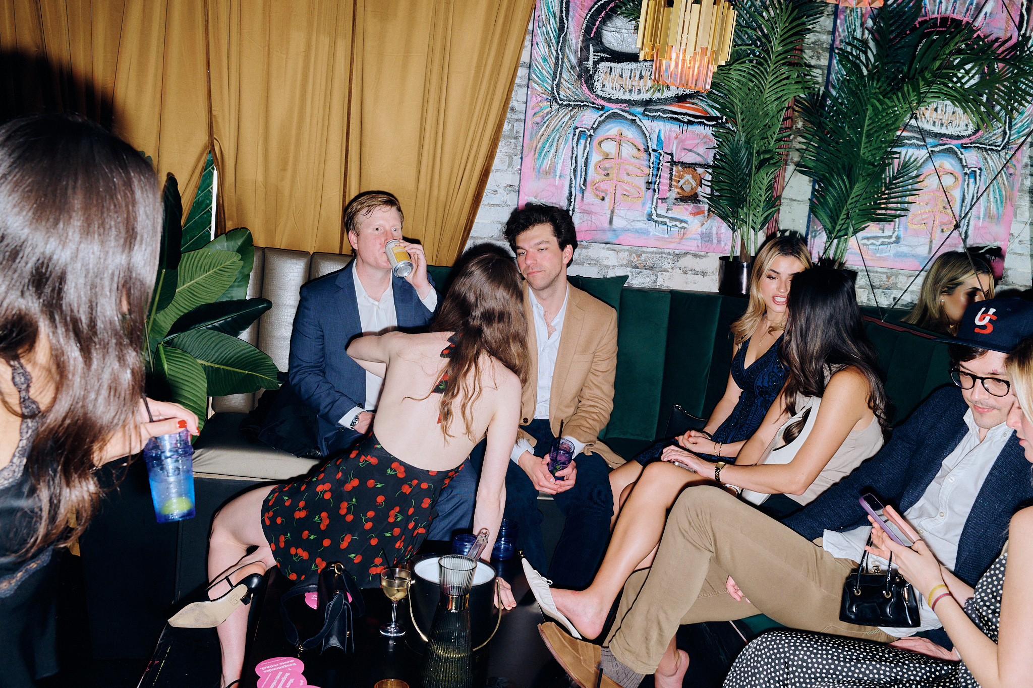 Young men and women socialize, drinking cocktails and canned beverages.
