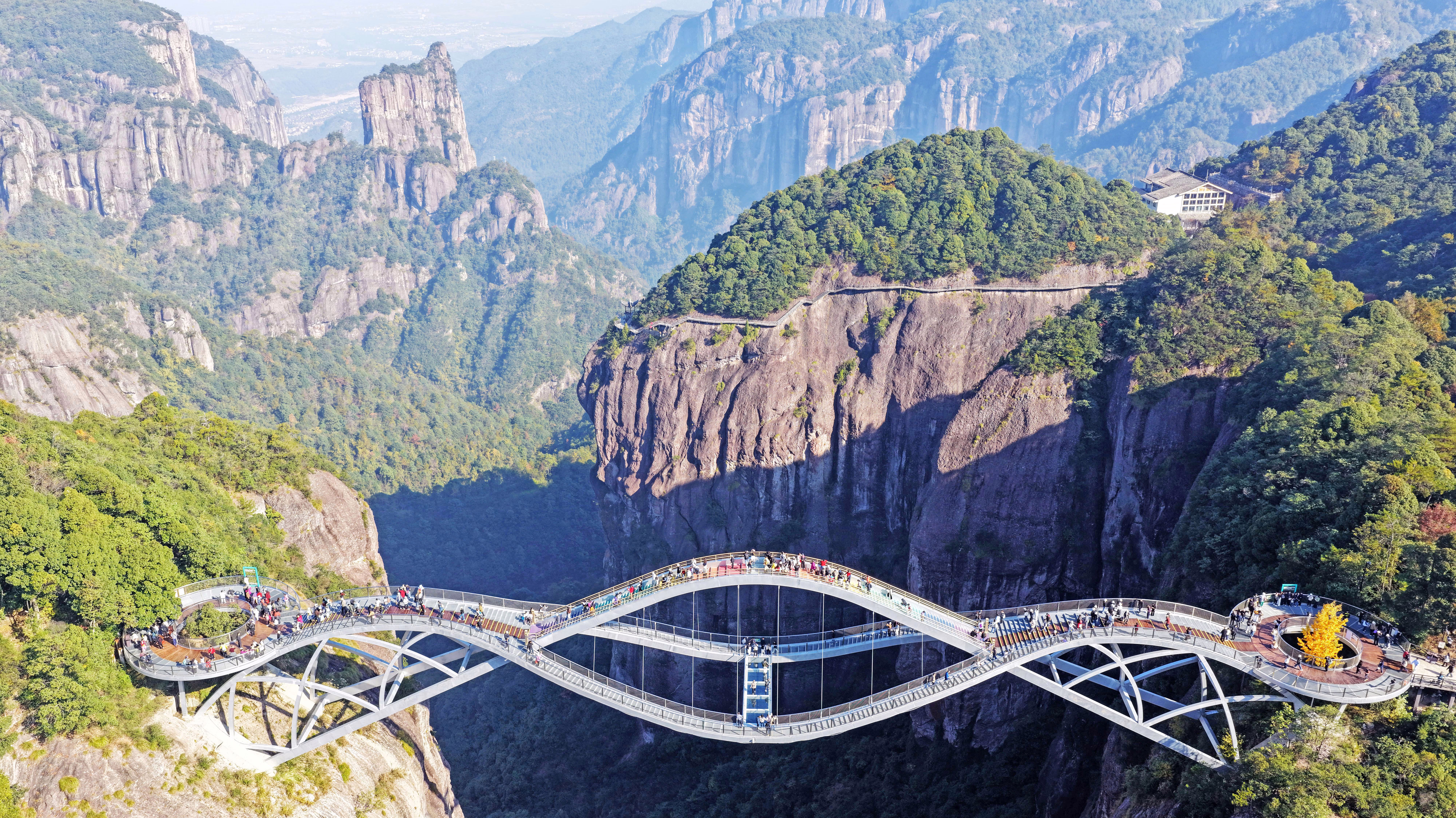 Tourists walk on an undulating glass-bottomed bridge over a steep valley.
