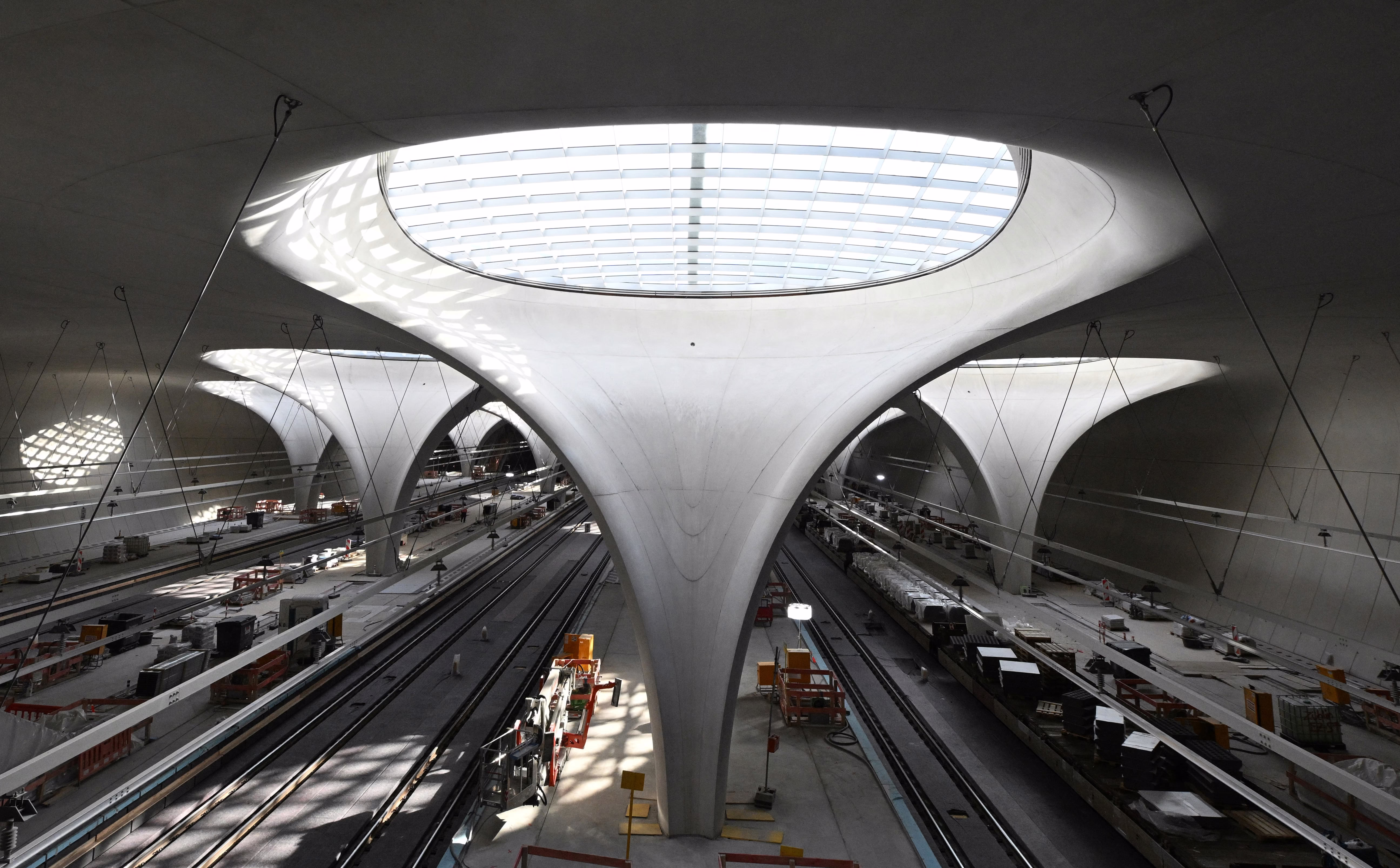 The interior of a modern train station under construction, featuring swooping pillars opening up to large circular skylights