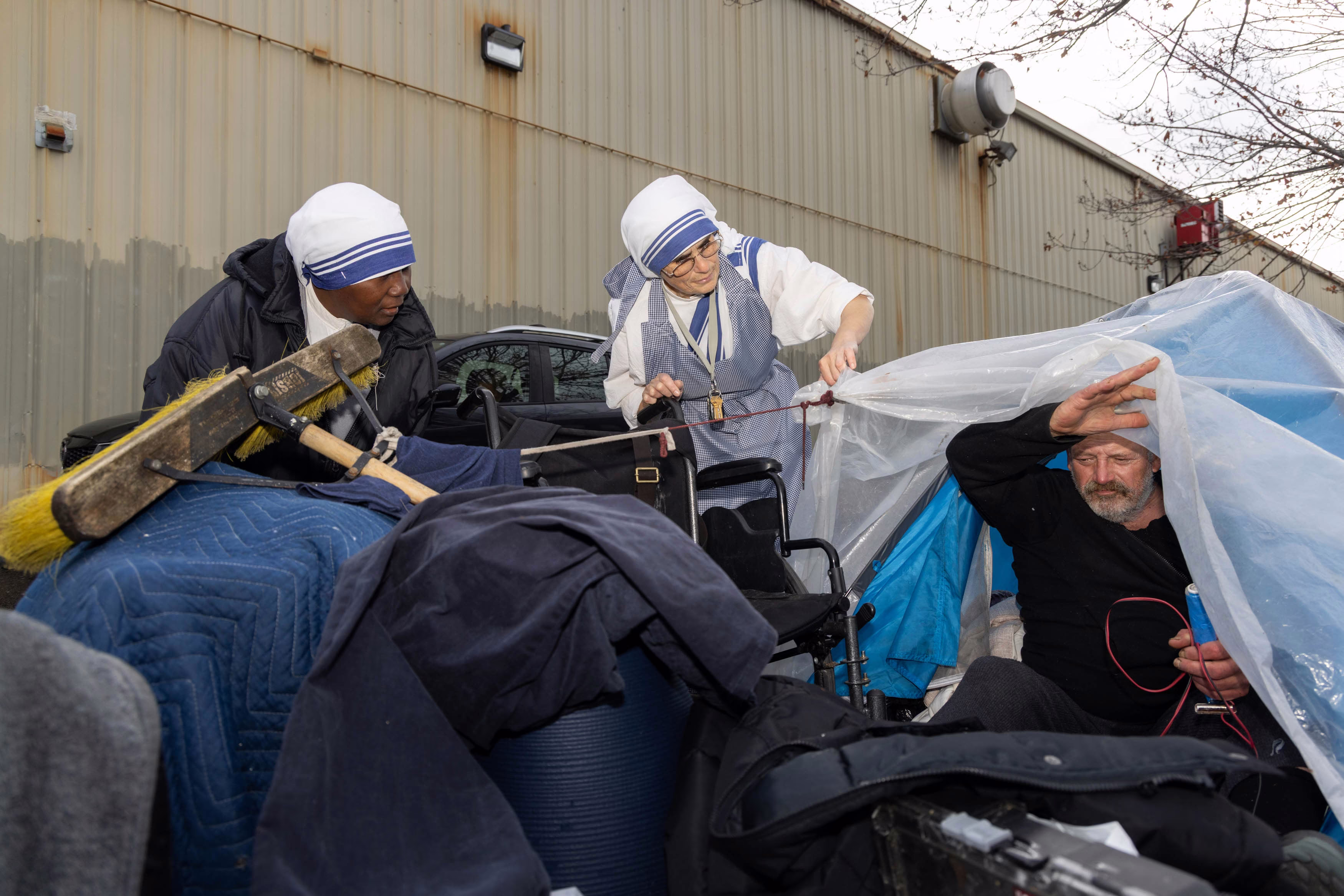 Picture of Sister Salvina and Sister Immaculate standing beside a tent on a city sidewalk, checking on one of their patients who lives there.