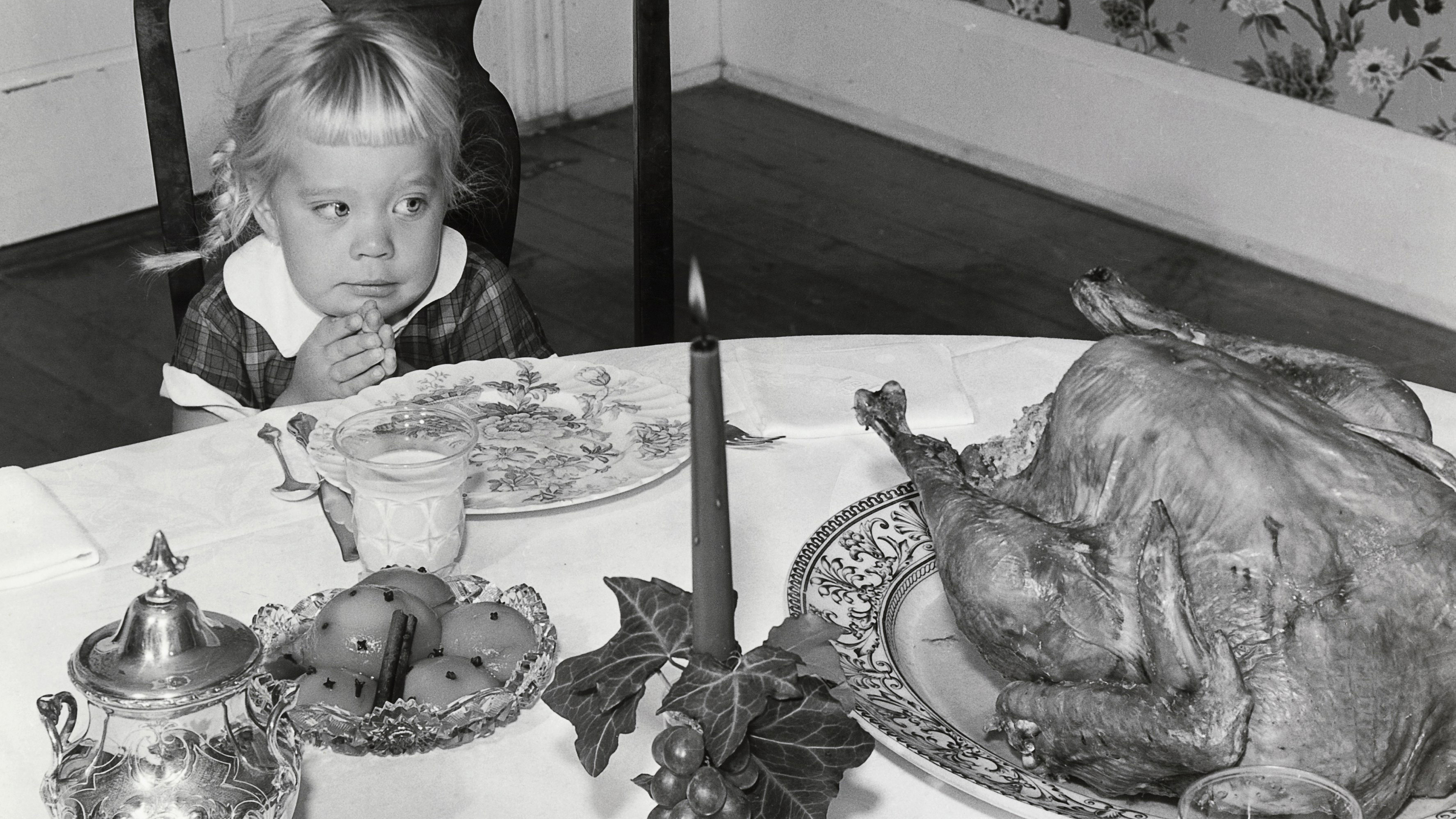 A young girl sits before a large roast turkey.