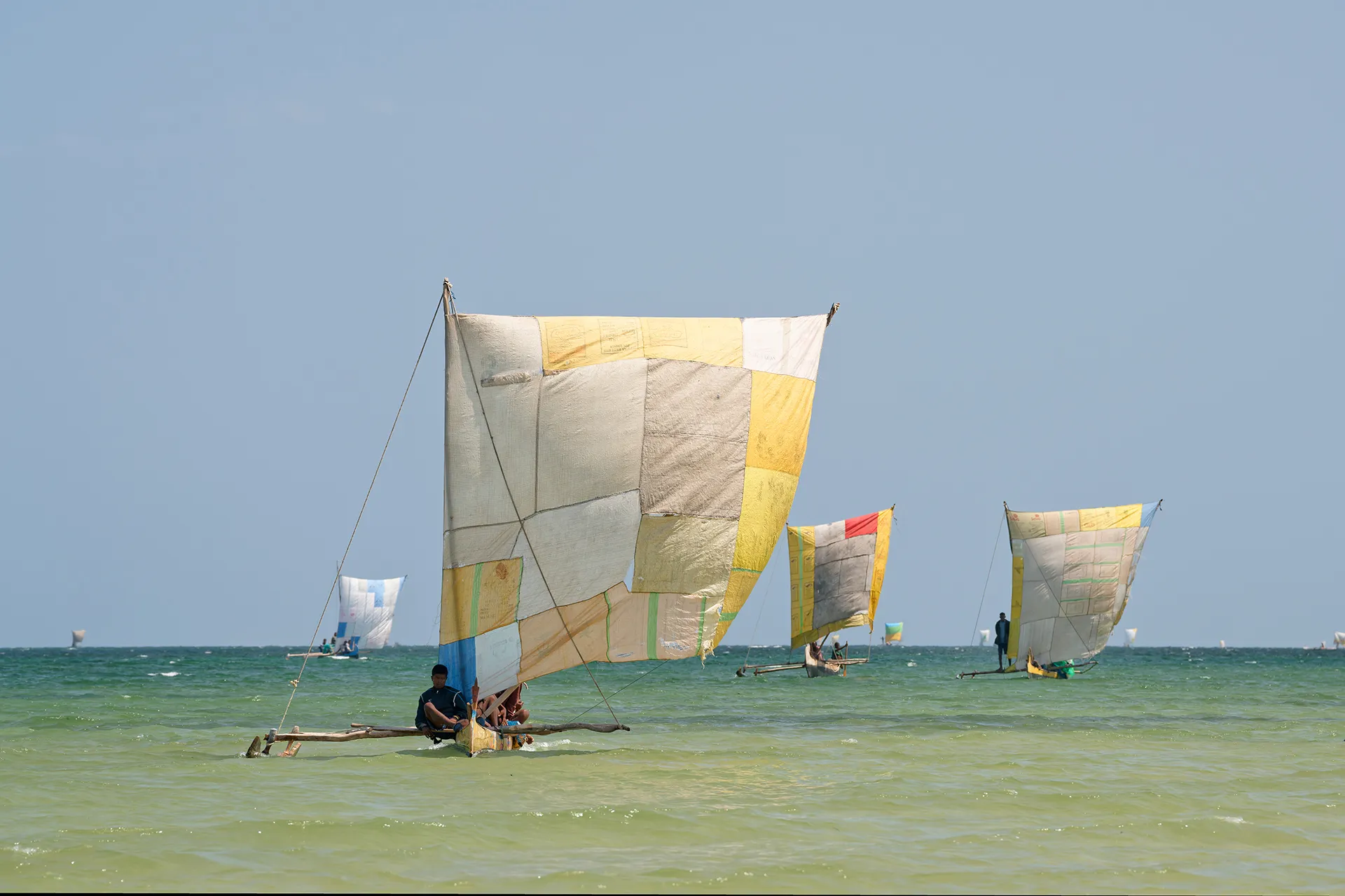 Malagasy fishermen sail in shallow waters with colorful-sailed pirogues.