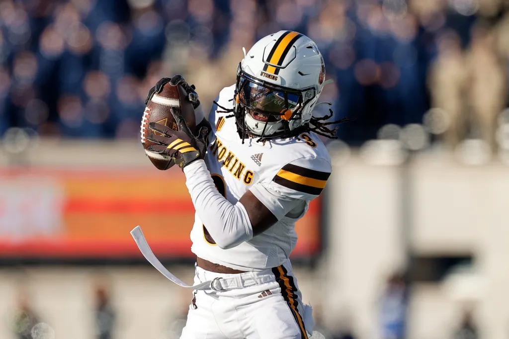 A Wyoming football player in a white uniform and helmet catching a football.
